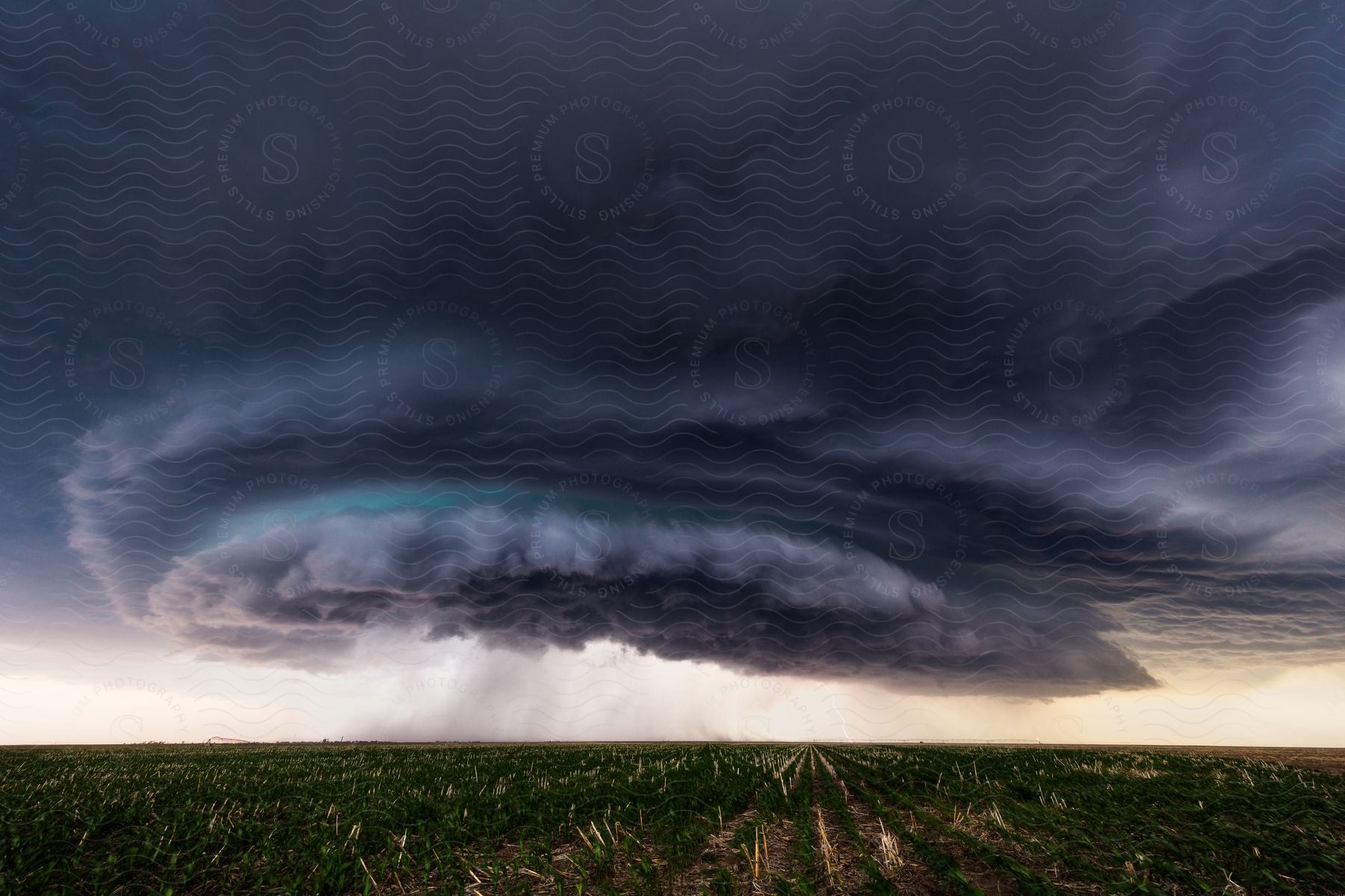 A dark supercell storm pours rain over rural farmland as it moves across the sky in southeastern colorado near two buttes