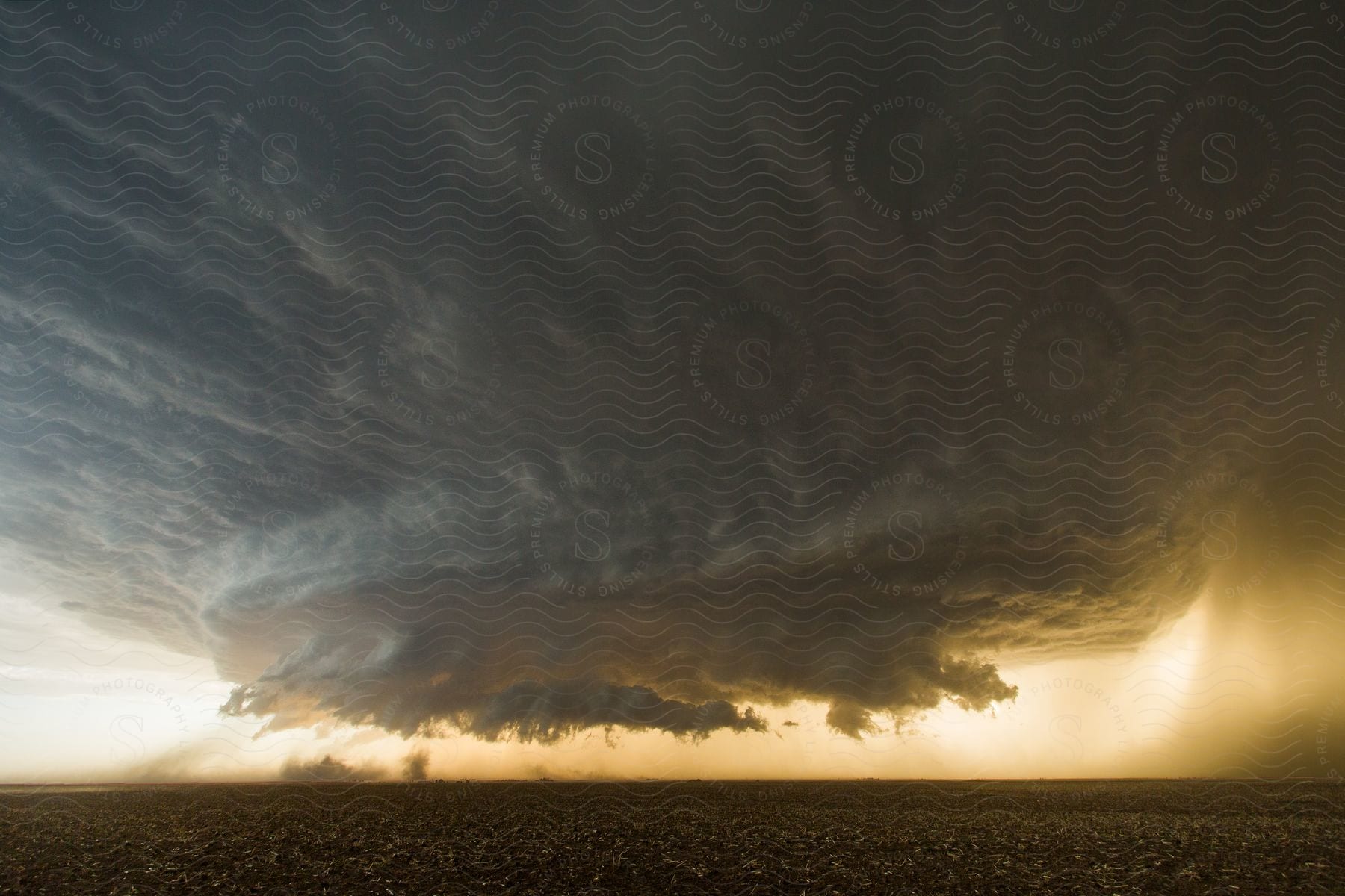 A dark supercell storm moves over rural farmland as rain pours down