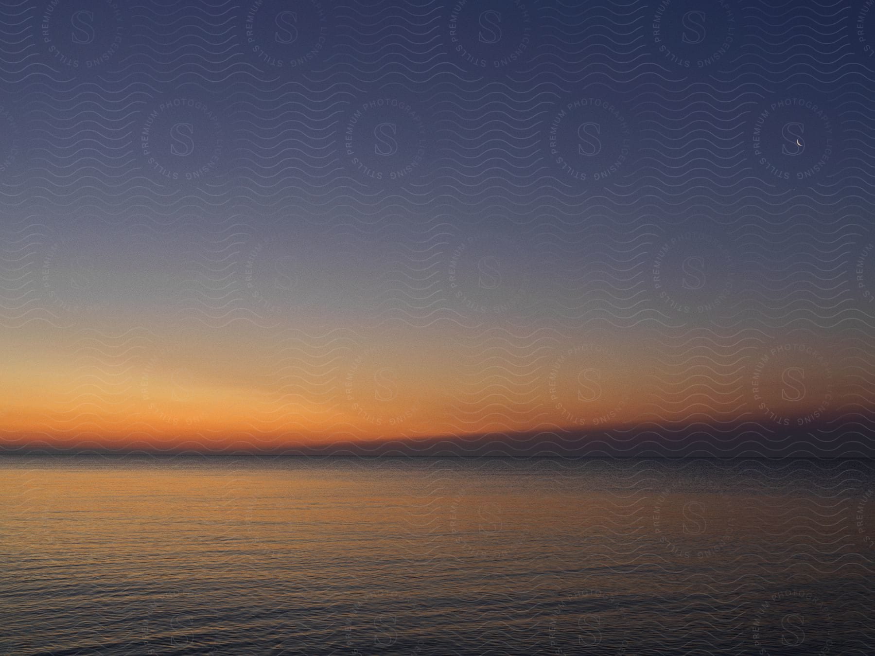 Waves roll across water with a red horizon after dusk