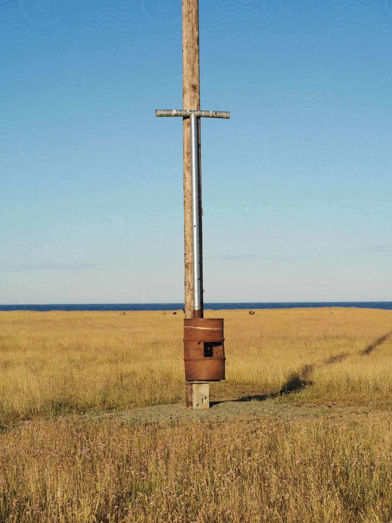 A rusted metal barrel attached to a telephone pole in a brown grass field