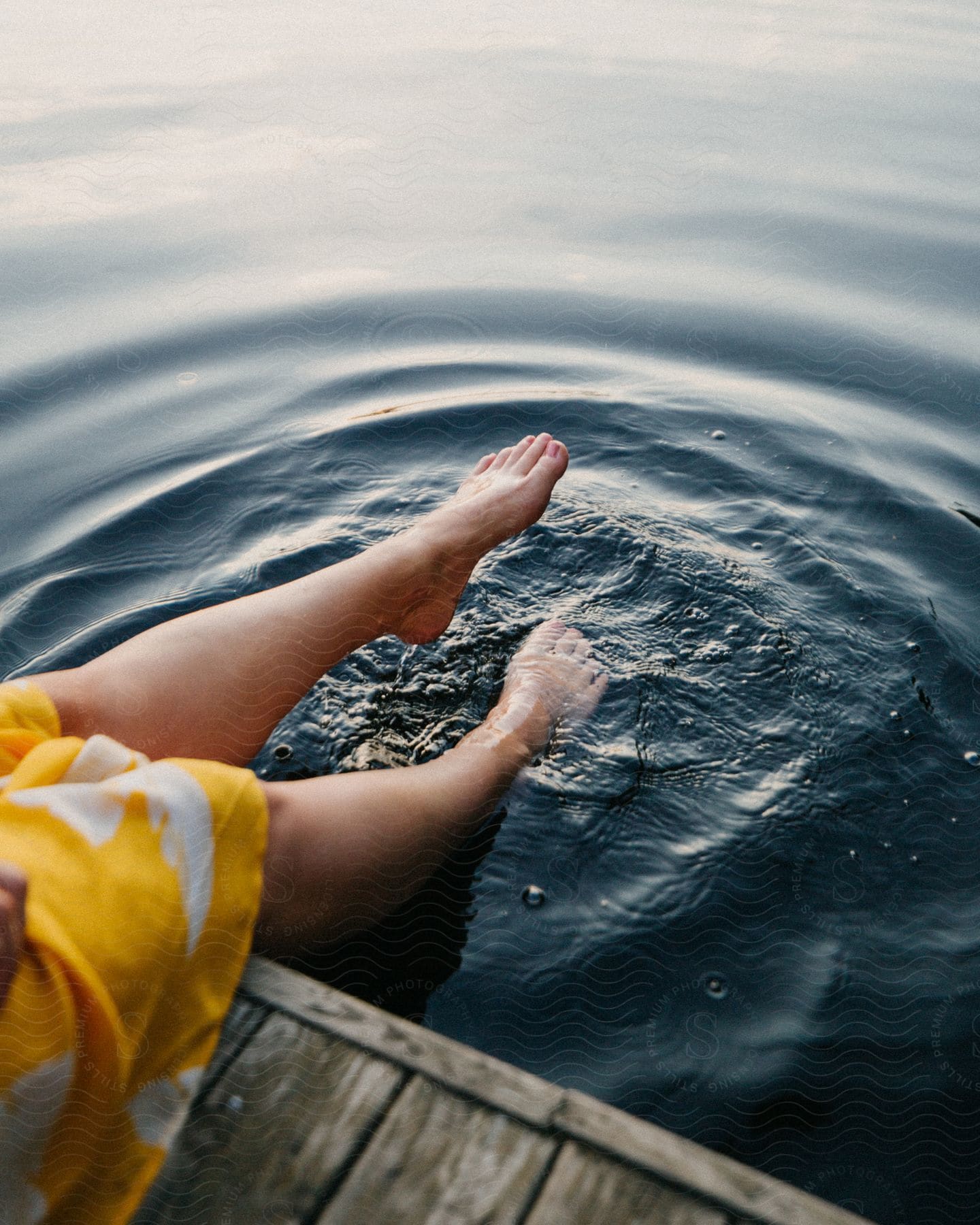 Woman sitting on a wooden dock kicks her legs in the water