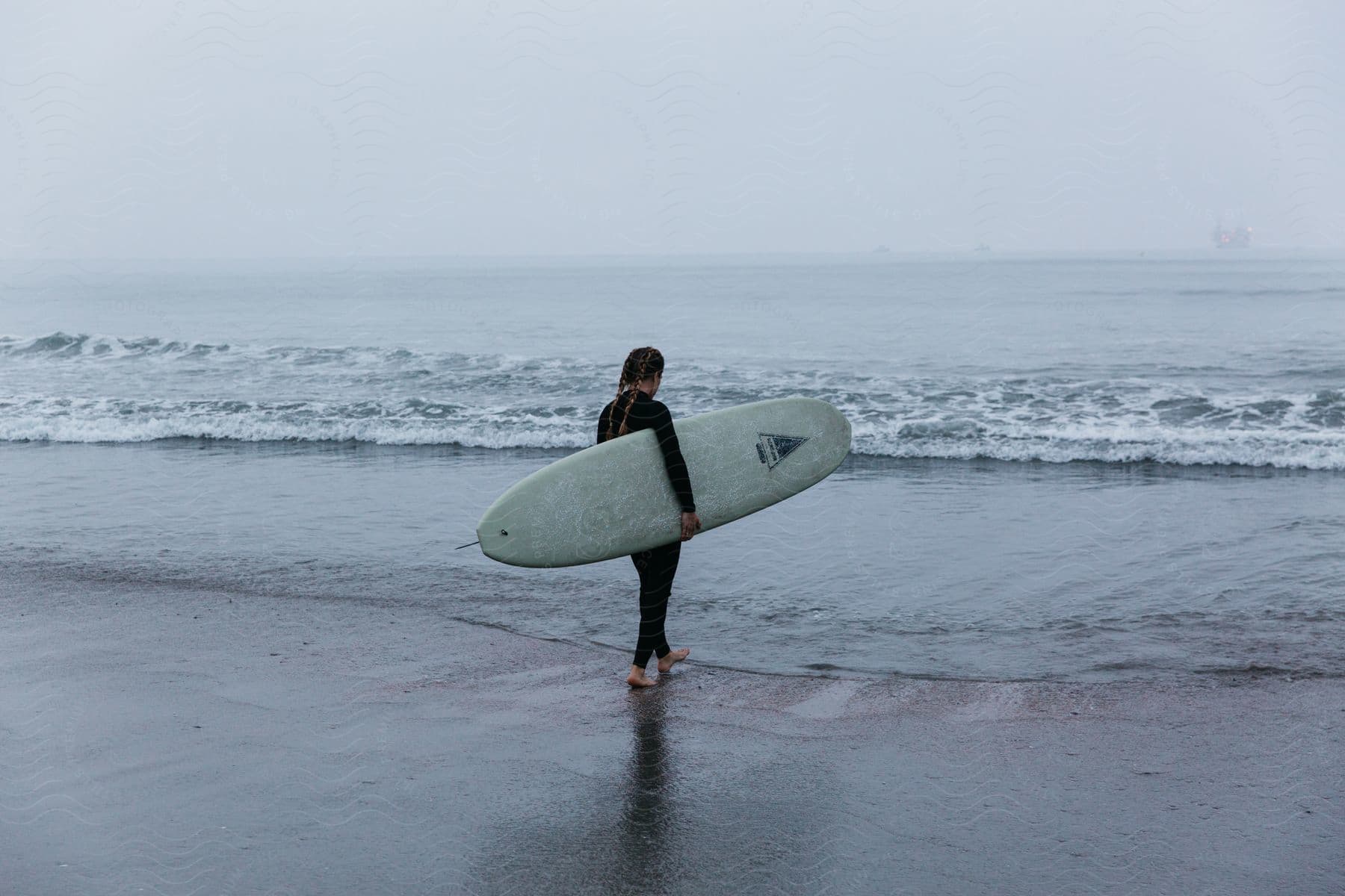 A woman excitedly walks towards the beach holding a surfboard under a cloudy sky