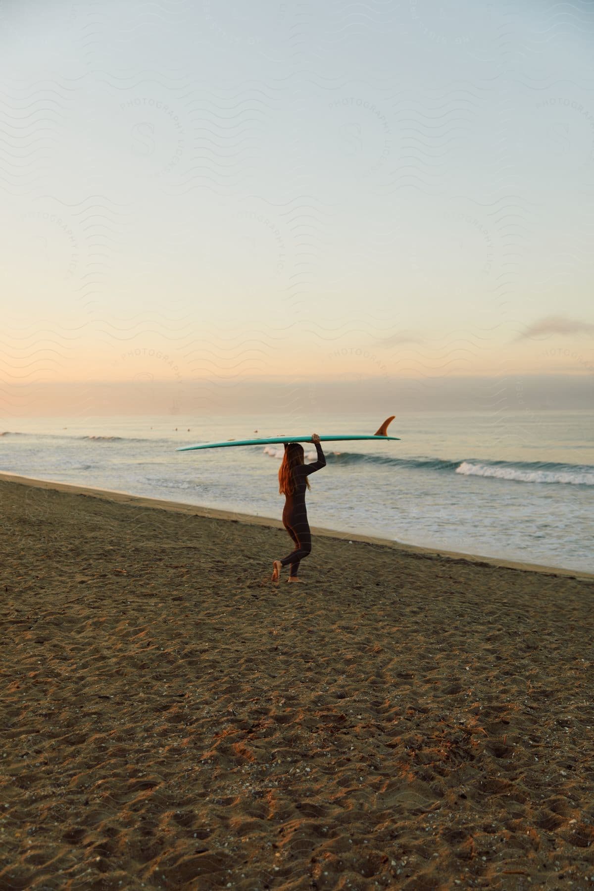 A woman walks to the water on the beach with a surfboard over her head