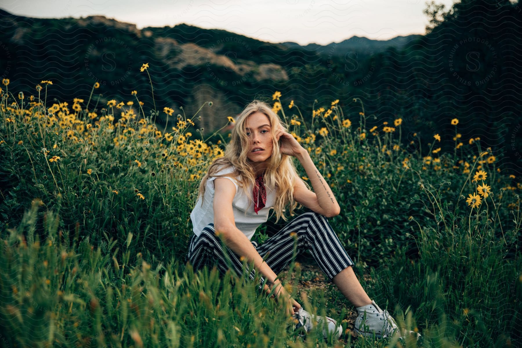 A blonde teenage girl sitting among vegetation with a neutral expression