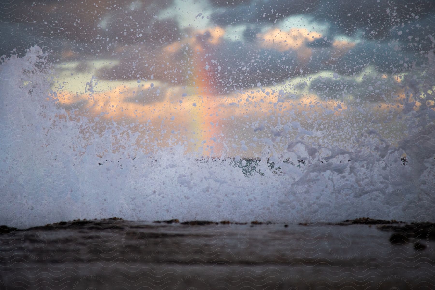 A landscape of ocean waves breaking against the shore with a rainbow in the distance