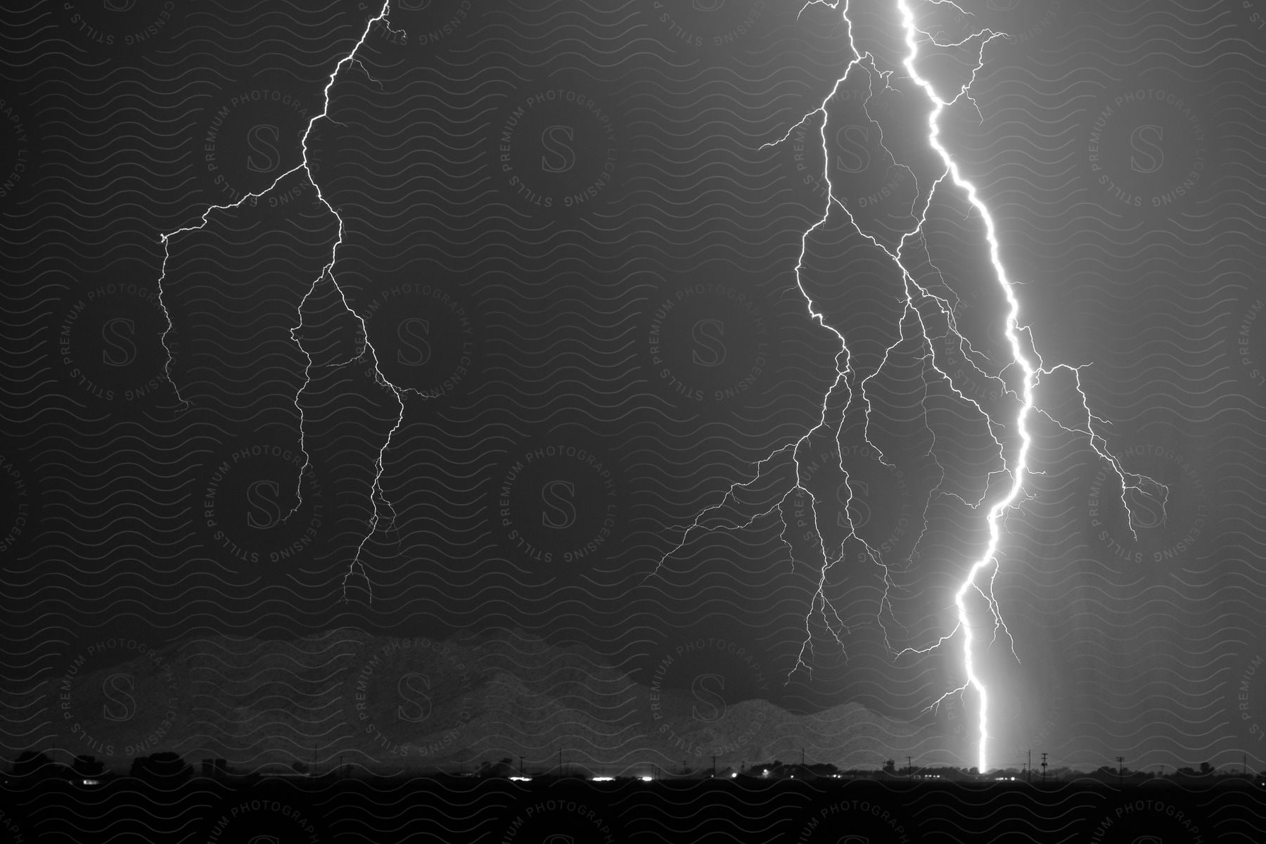 Lightning striking near a town in the countryside at night captured in black and white