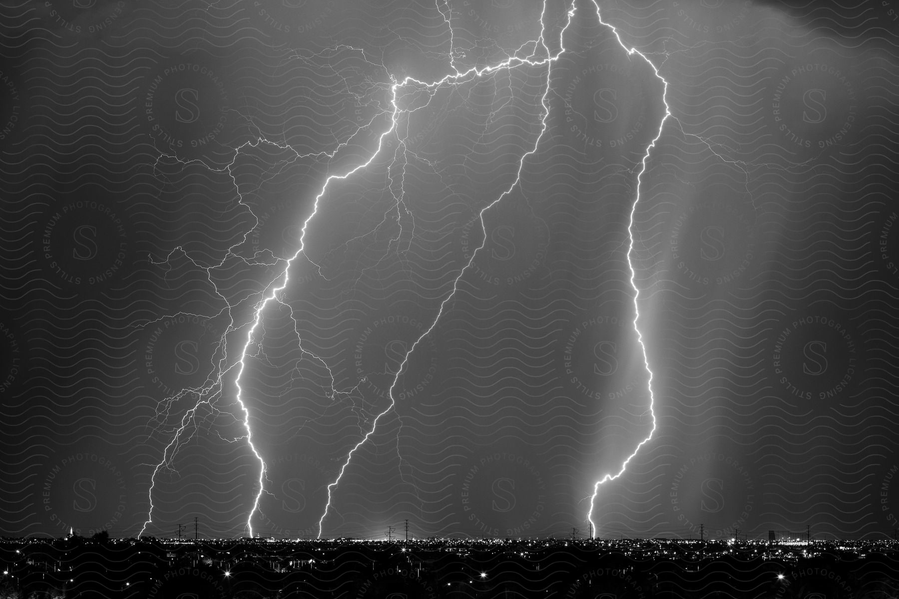 A lightning storm illuminates a city at night as buildings light up the streets below