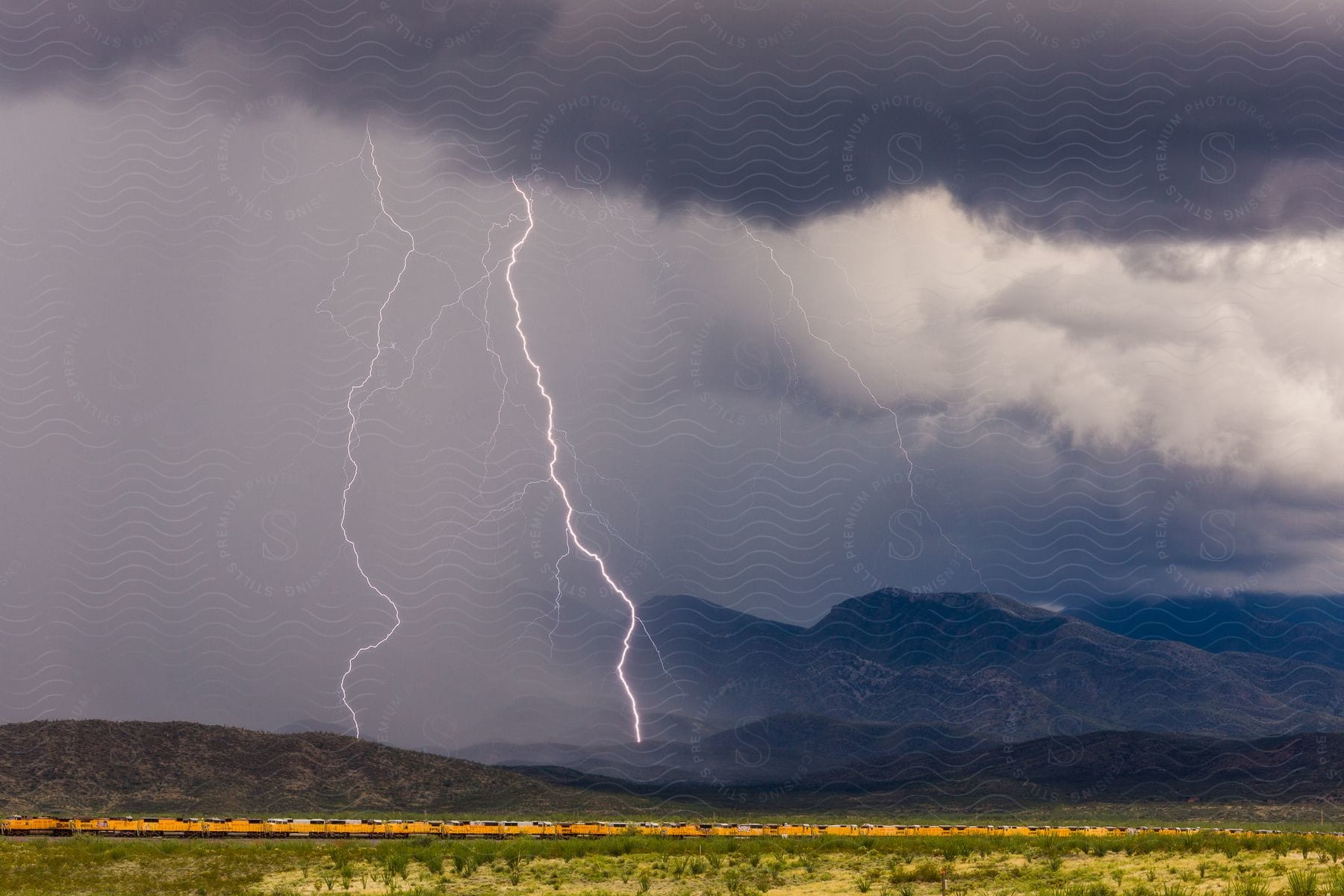 Lightning strikes over mountains as a yellow train passes in the desert