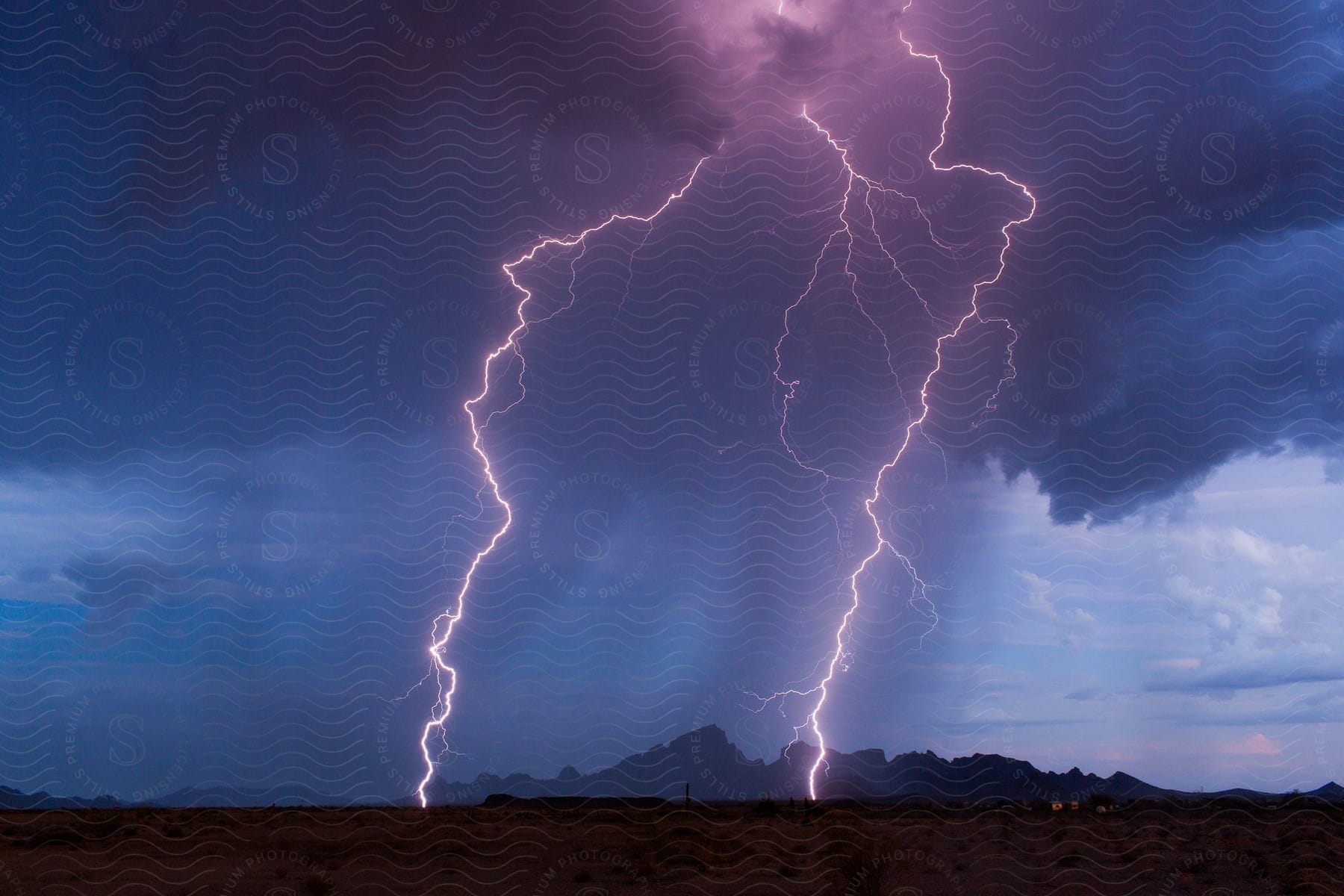 Storm rages on with purple lightning illuminating dark clouds over mountain