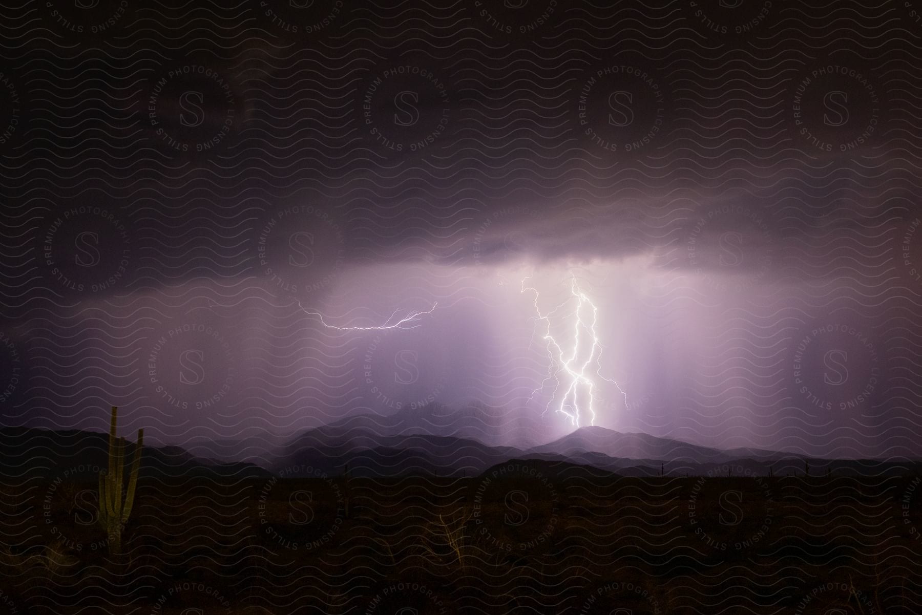 Dark storm clouds pour rain over the desert and lightning illuminates the night sky over mountains