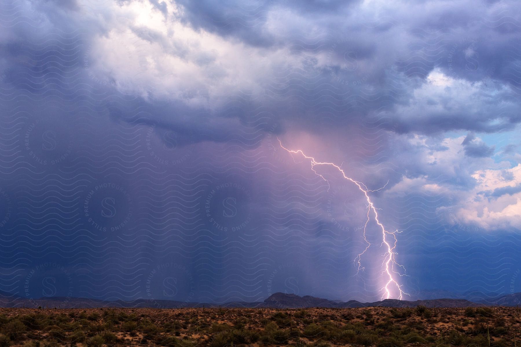 Lightning and rain falling from storm clouds over the mountains in the plains