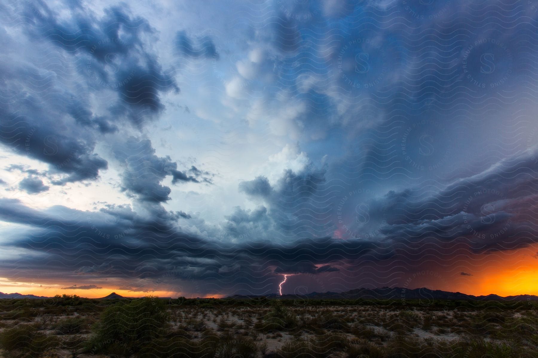 Dark storm clouds hang over the desert as lightning strikes over the mountains