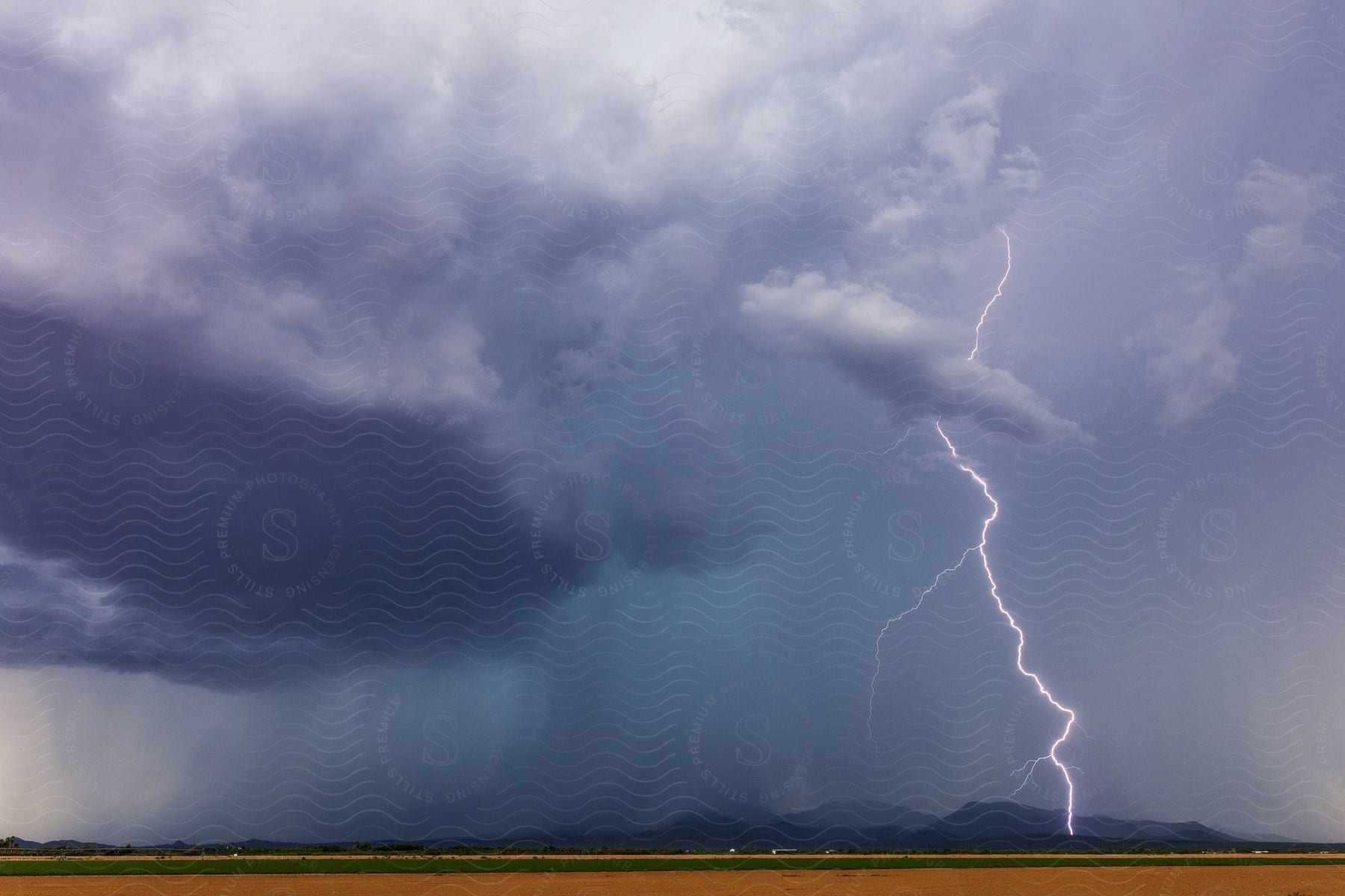A lightning bolt strikes in the table top mountains west of stanfield arizona with large dark clouds over a field