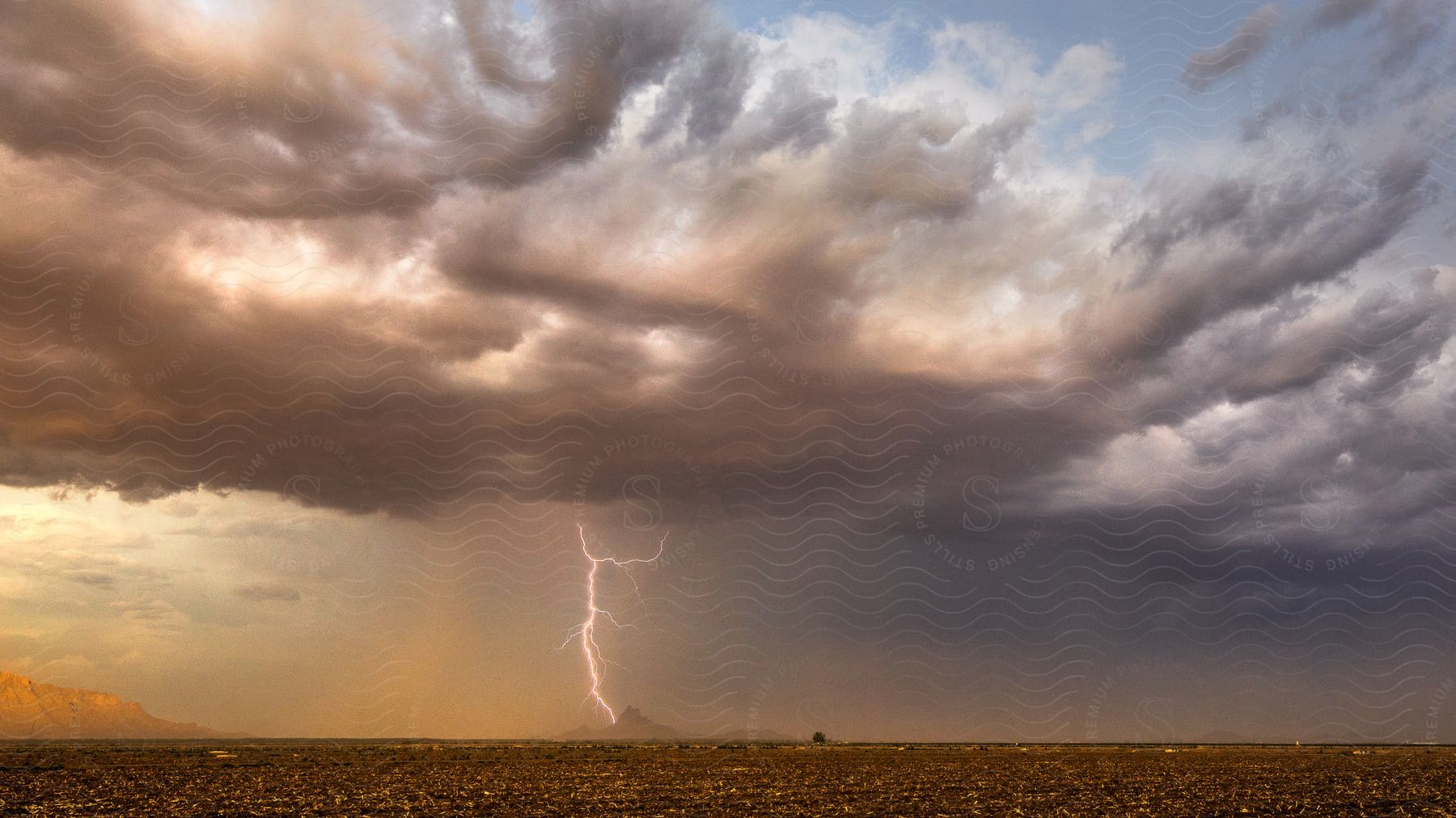 A storm cloud moves over rural farmland and lightning cracks the sky as rain pours down