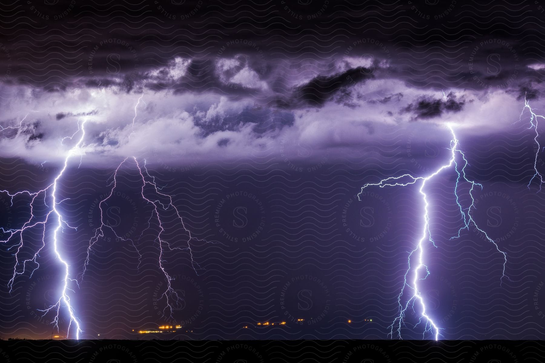 Multiple lightning bolts hit the ground around a town in the plains at night