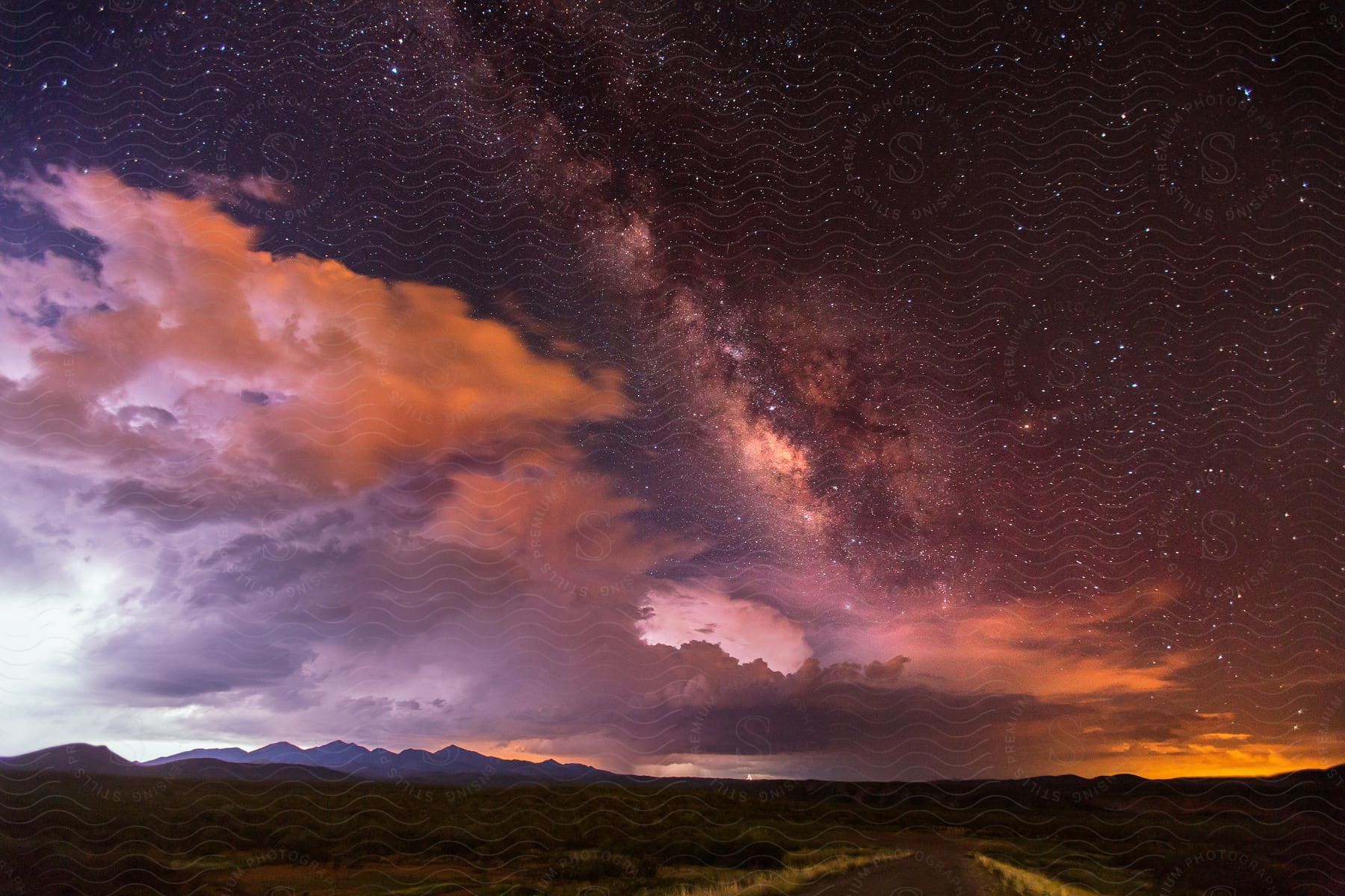 A clear night sky with a thunderstorm in the distance and the milky way shining overhead