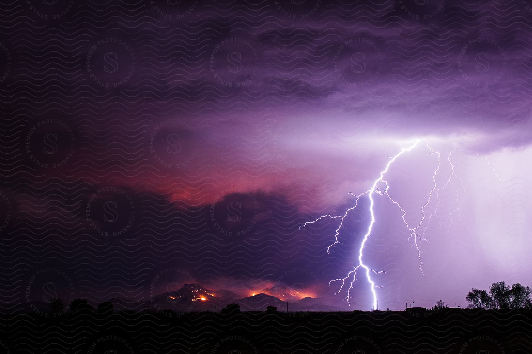 Bolts of lightning flash across a sky near a mountain burning from a wildfire in arizona