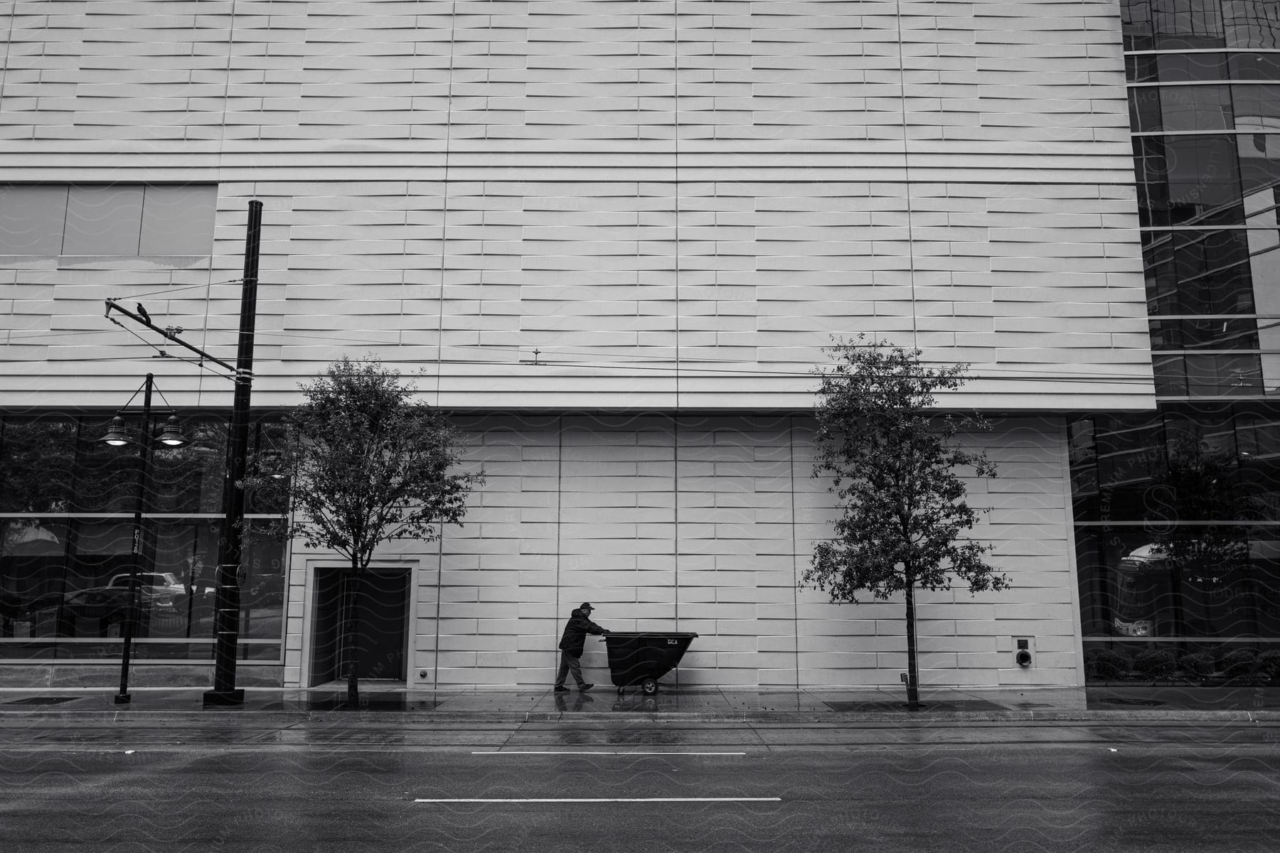 A Man Walking In Front Of A Tall Building With A Trash Container