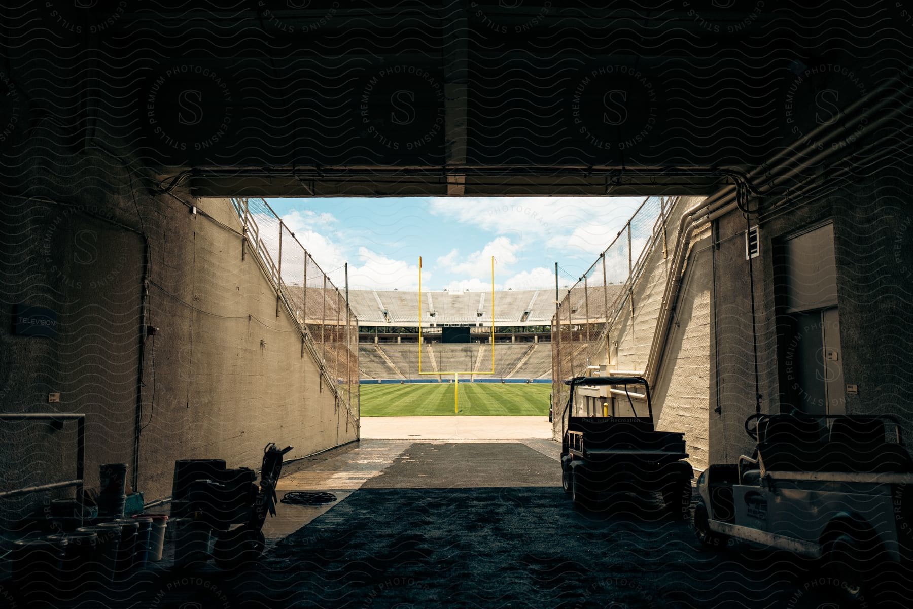 Blue sky with sun and white clouds over a football stadium as seen from inside the locker room tunnel entrance