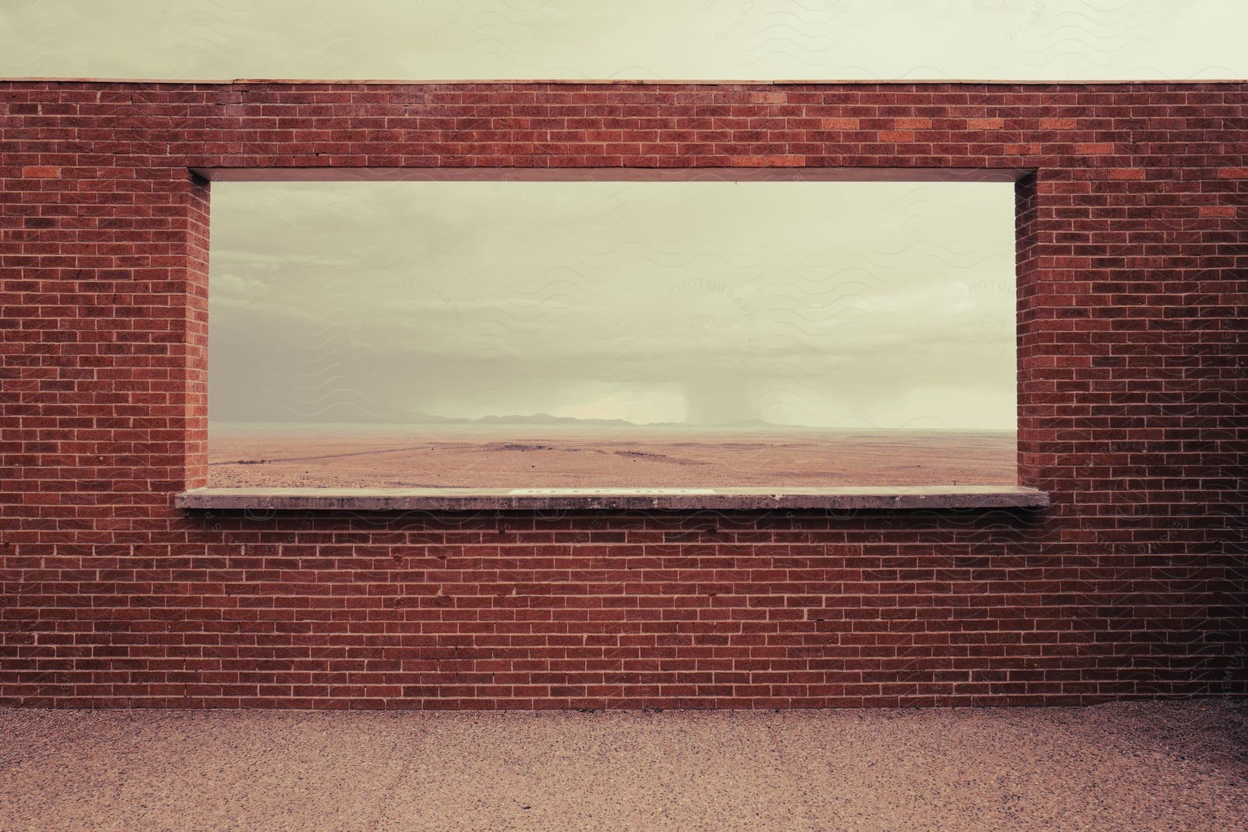A brick wall with a window framing a desert landscape during a storm