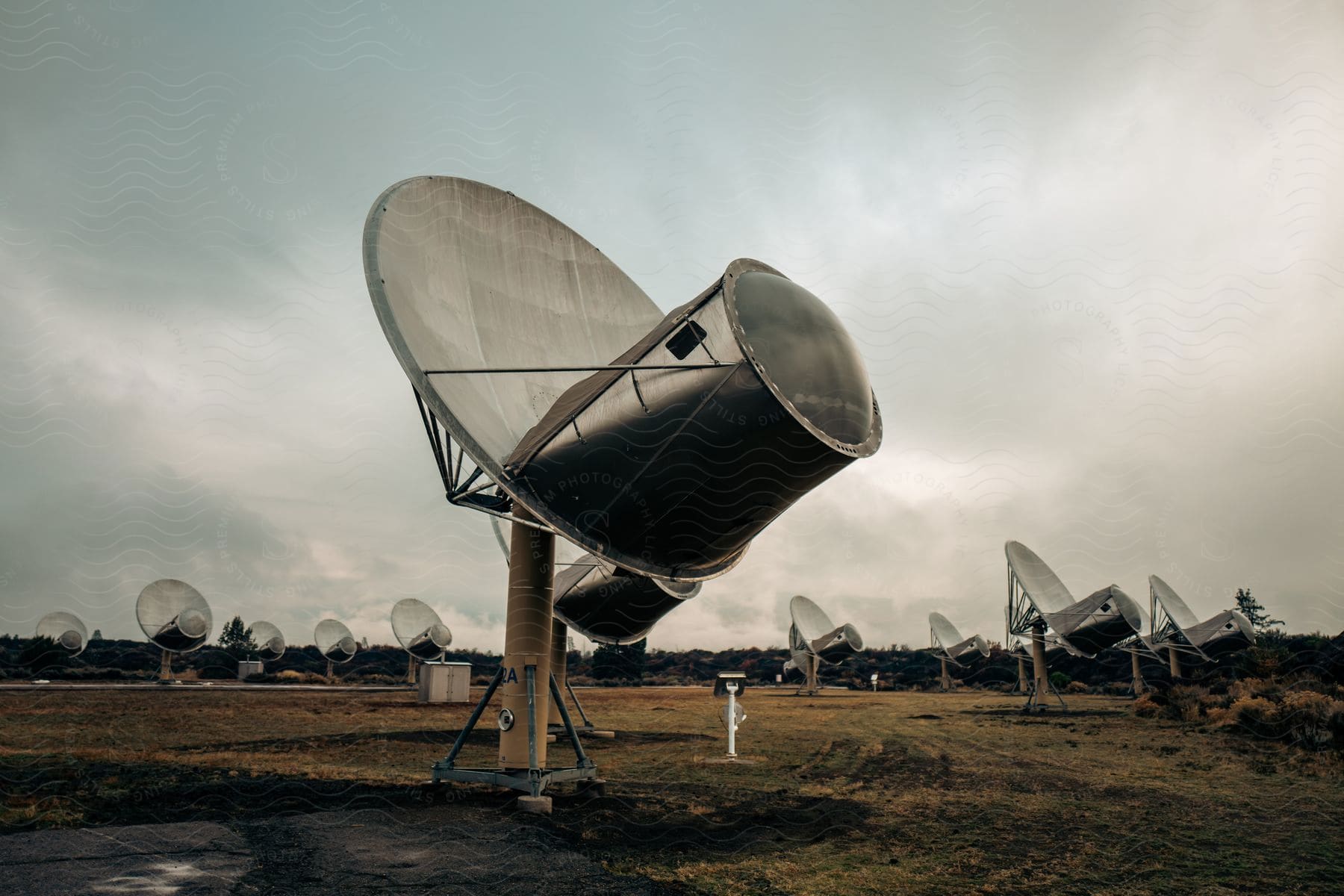 An array of dish satellites in a large field on a cloudy day