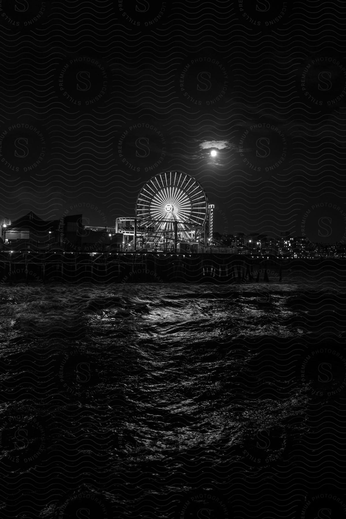 A well lit ferris wheel on a pier under a full moon near the water