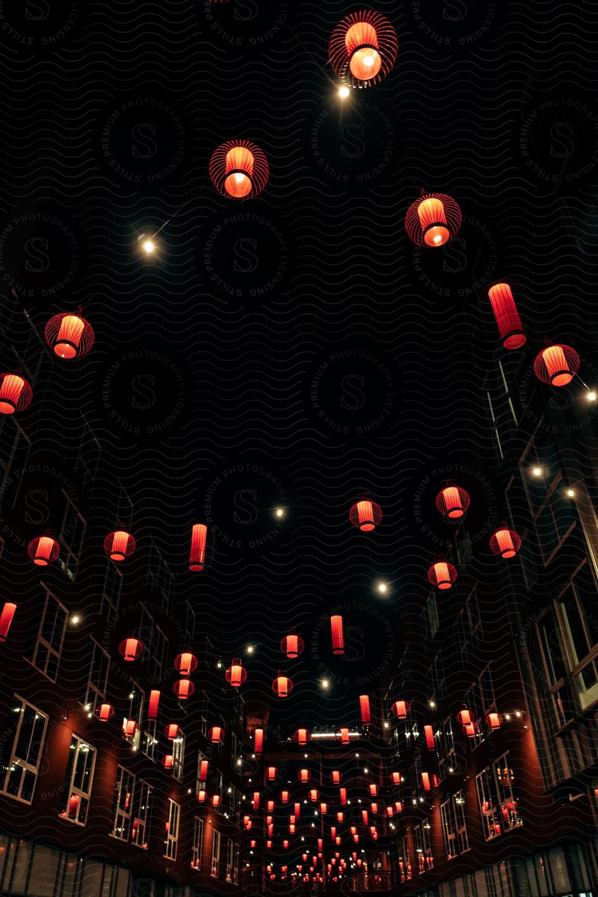 Zigzagged lanterns with orange covers and tops hung across a street lined with brick buildings and lots of windows at night