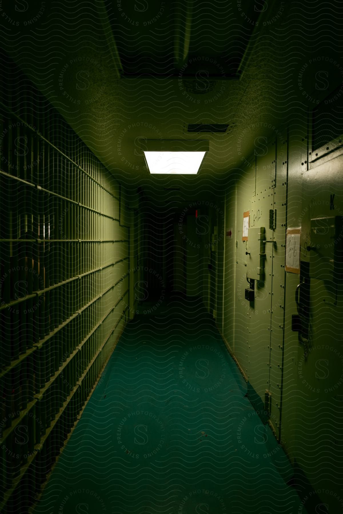 A jailhouse corridor with electric panels on the wall and bars on the cell block