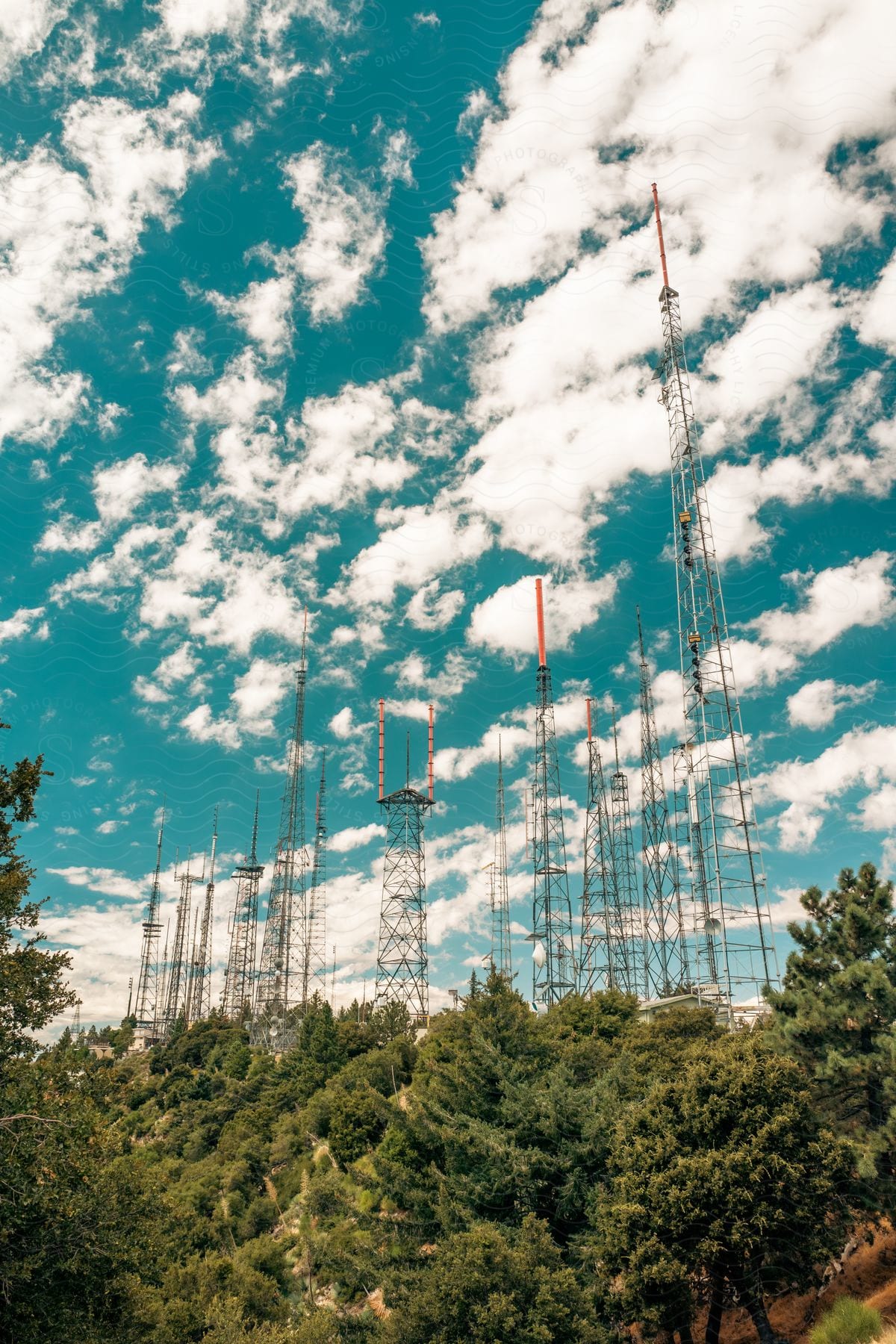 Electricity power station towers stand tall above a forest of trees under a blue sky with scattered clouds during the day