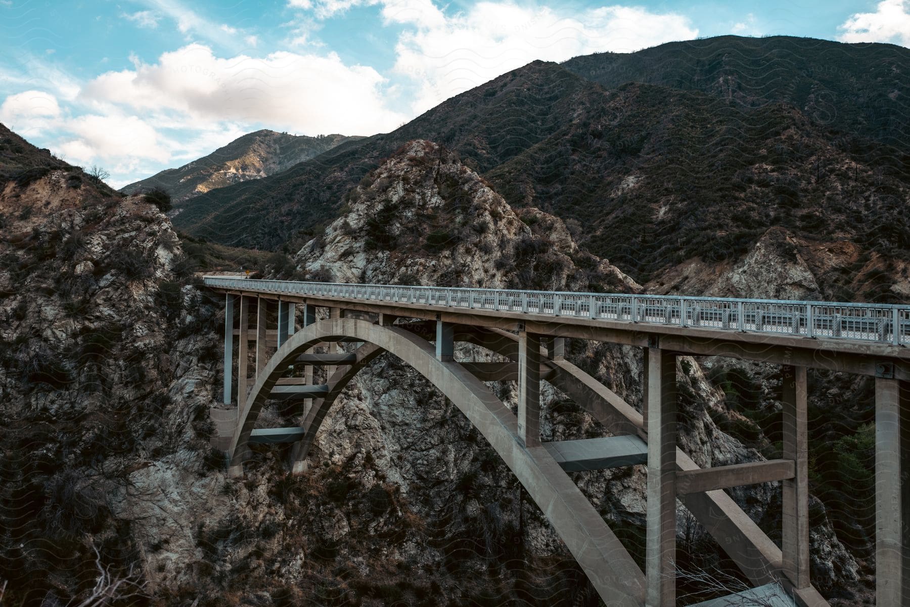 A bridge stretches across a mountain valley and into the mountains in the outdoors during the day