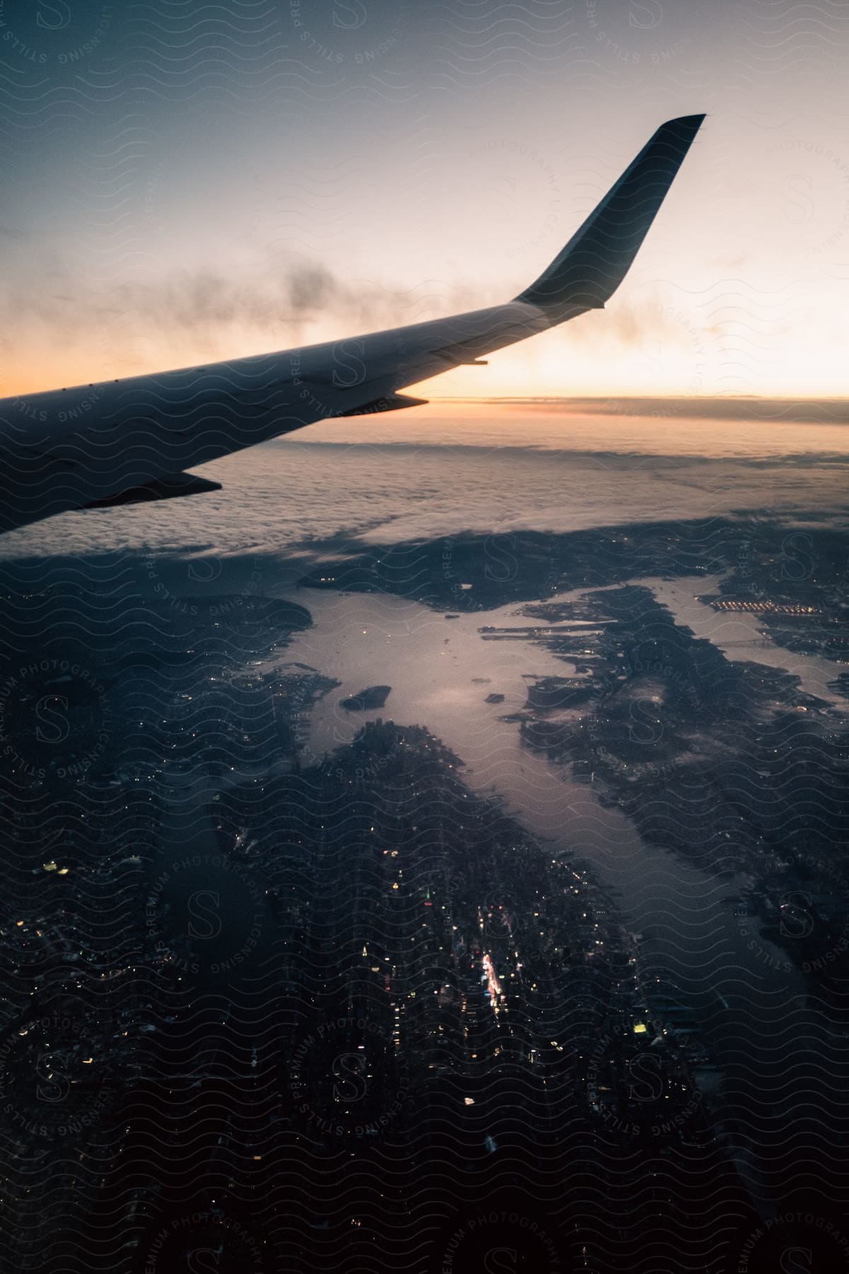 A city harbor lights up at night under a cloudy sky viewed from under an airplane wing