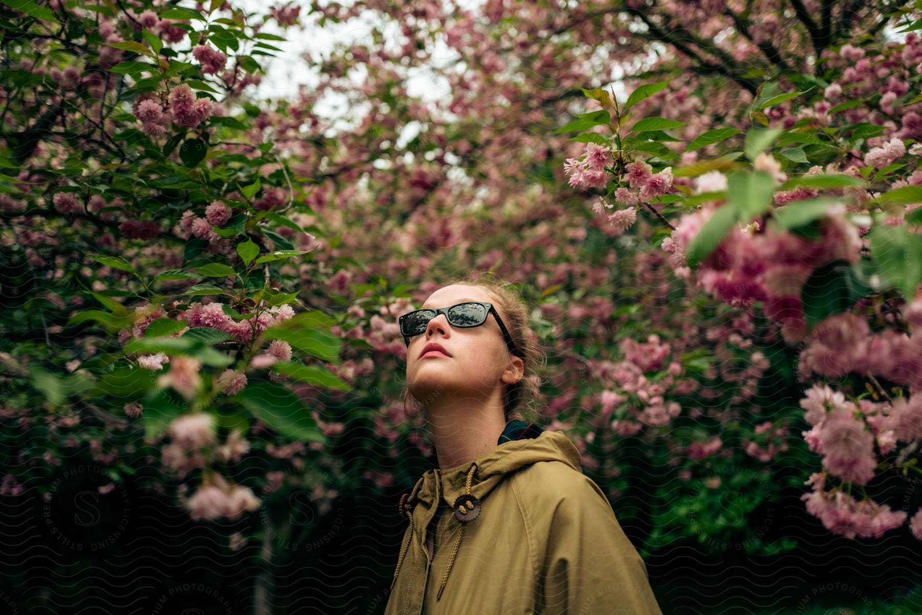 A girl wearing a fall jacket walks under flower vines and trees in a forest