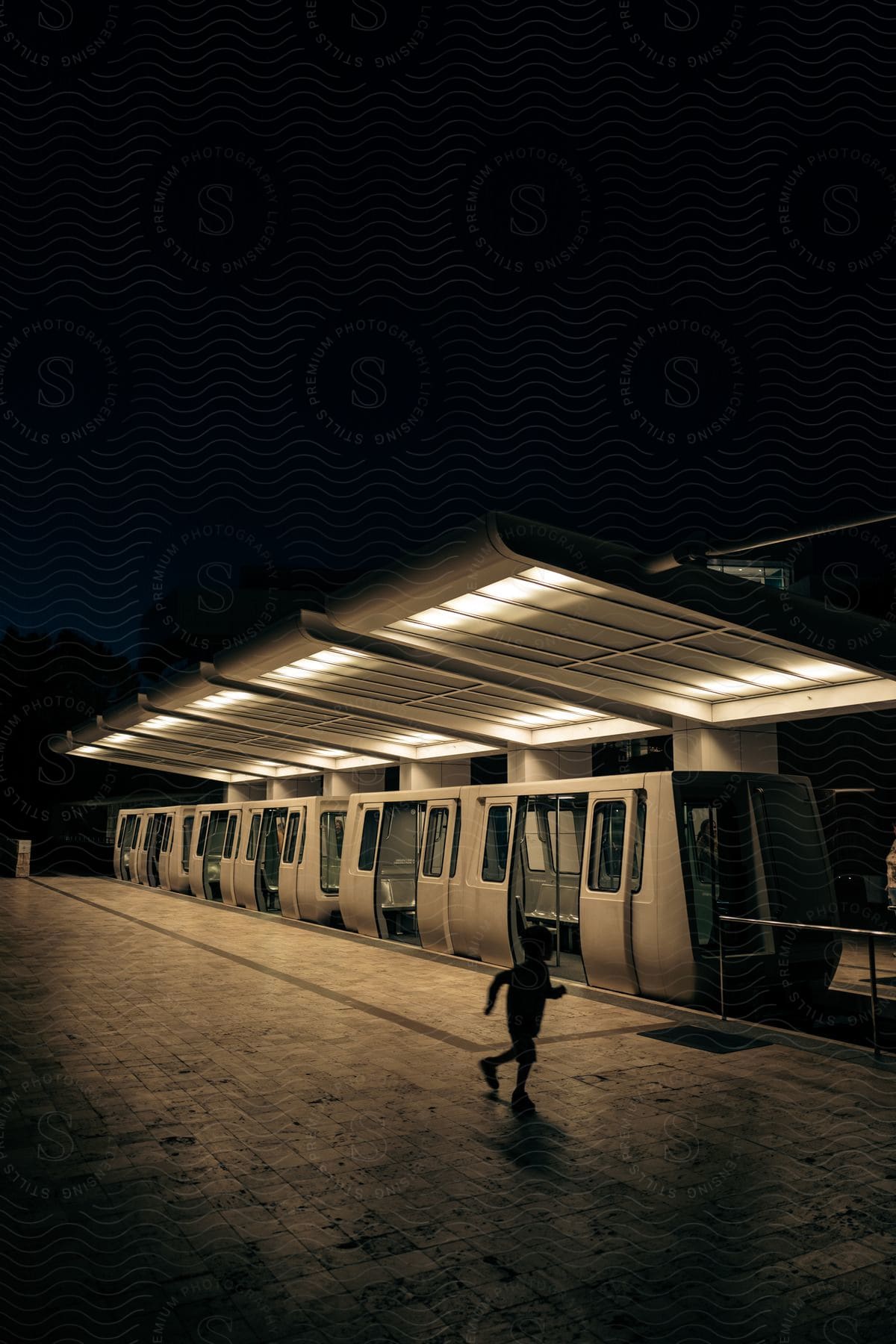 A modern train parked in a train station at night with a child running towards it