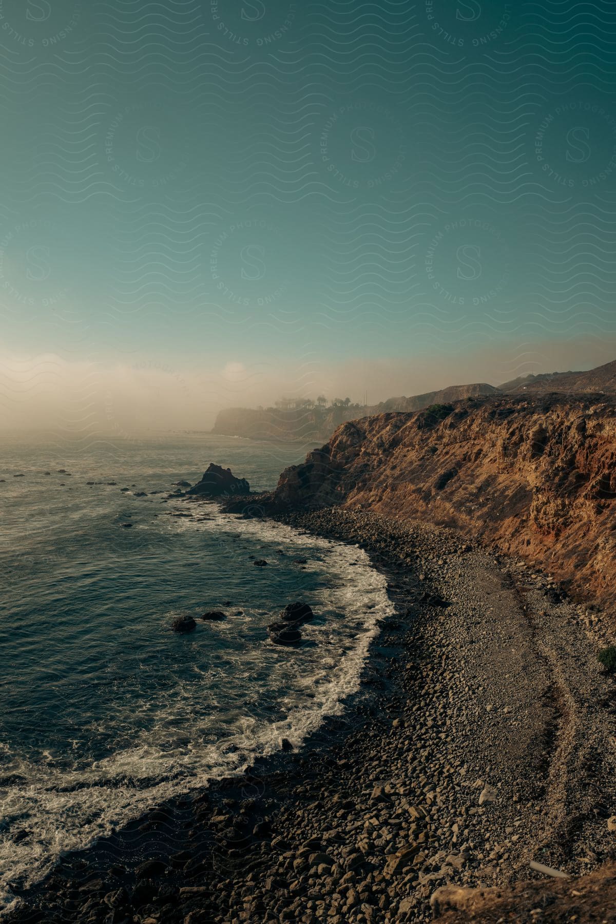 Stock photo of waves crash against a rocky beach surrounded by cliffs on a hazy day