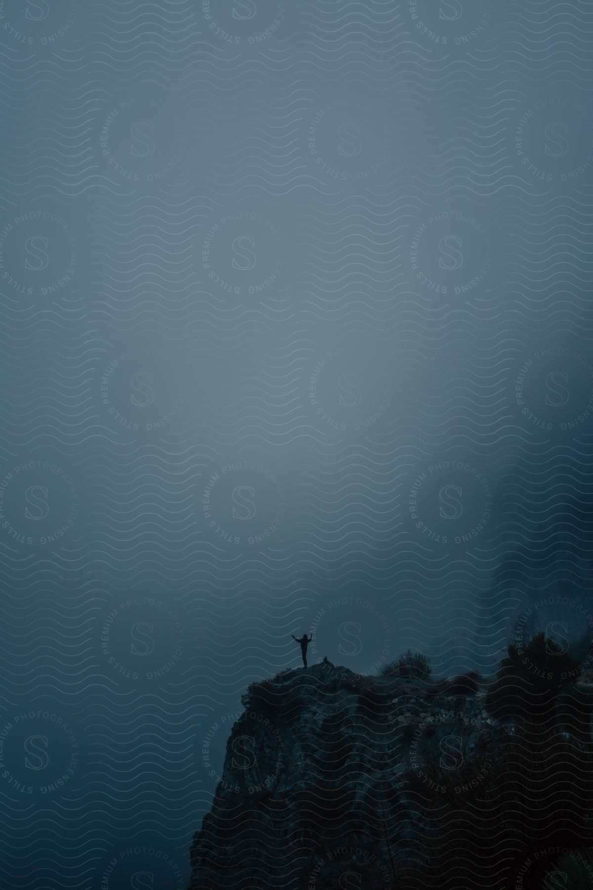 A person stands near a foggy mountain ledge at dusk