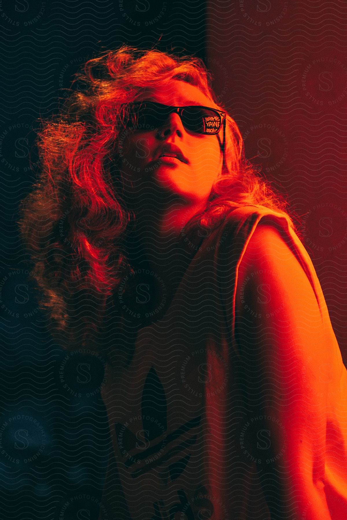 Stock photo of blonde girl wearing dark shades looking up under the orange glow of lights in the dark