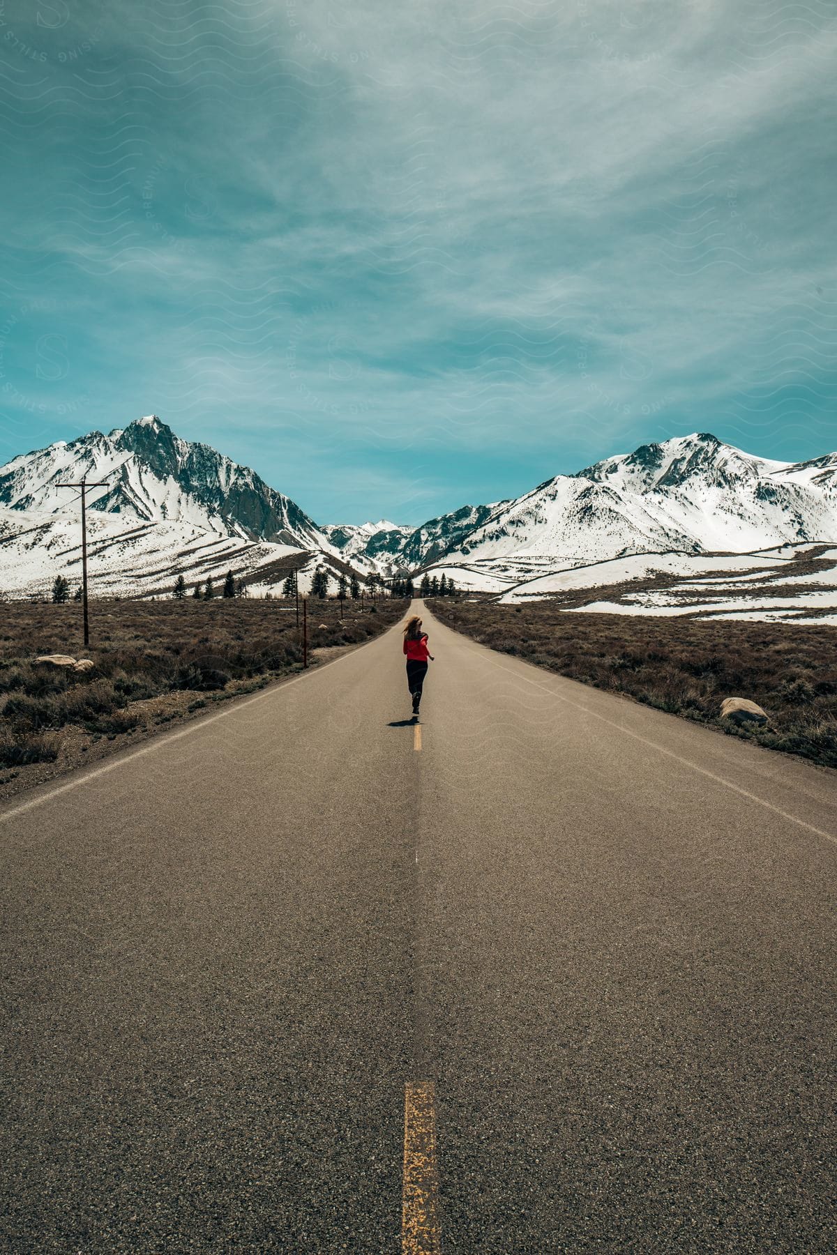 A woman running on a road with vegetation and mountains with snow on the horizon