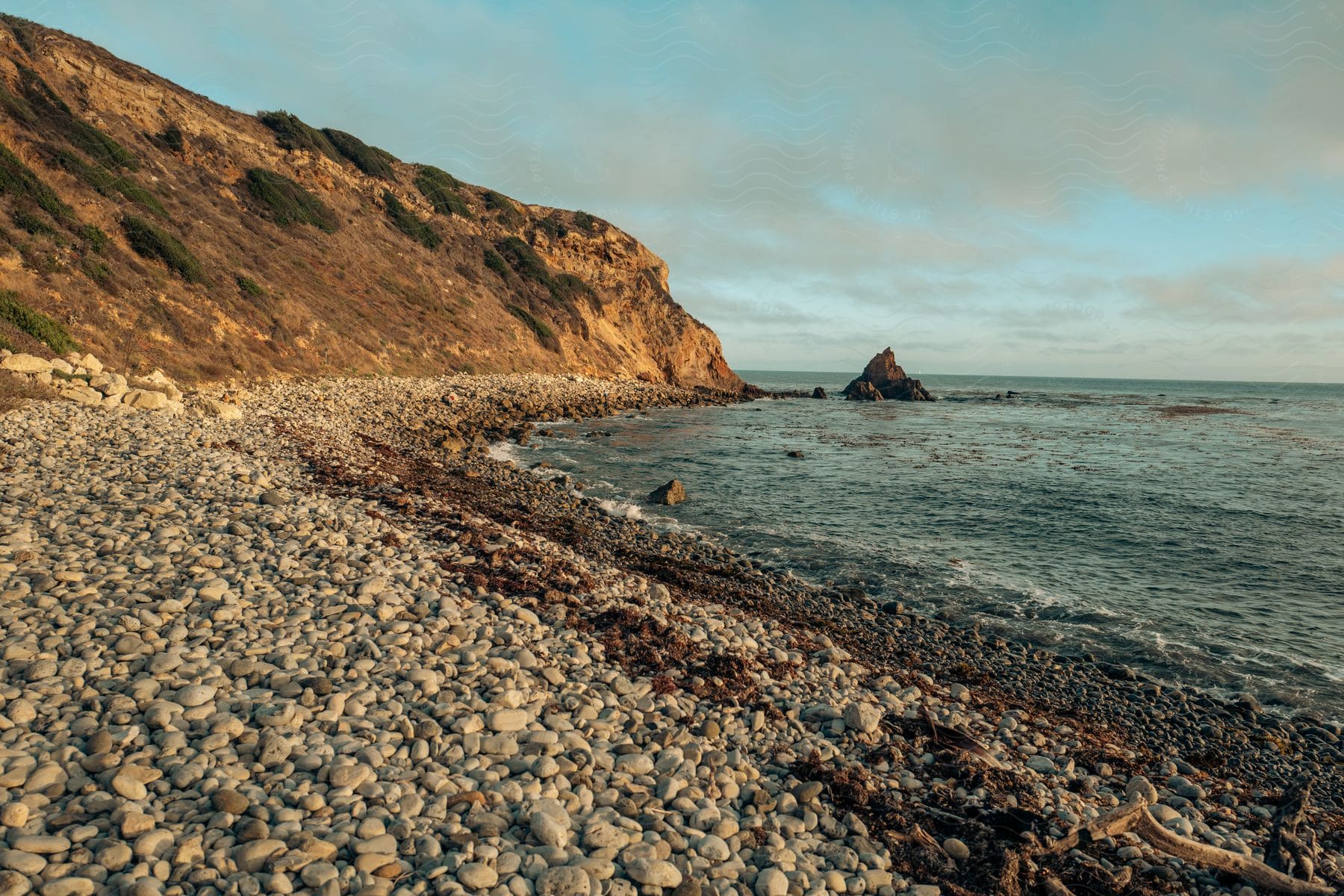 A sunny day by the ocean with a natural landscape clouds and a rocky shoreline