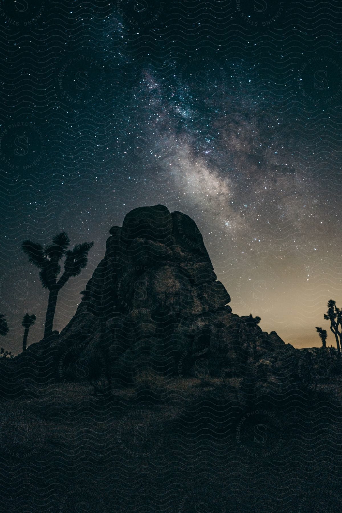 The milky way shines above a rocky mountain and trees at night