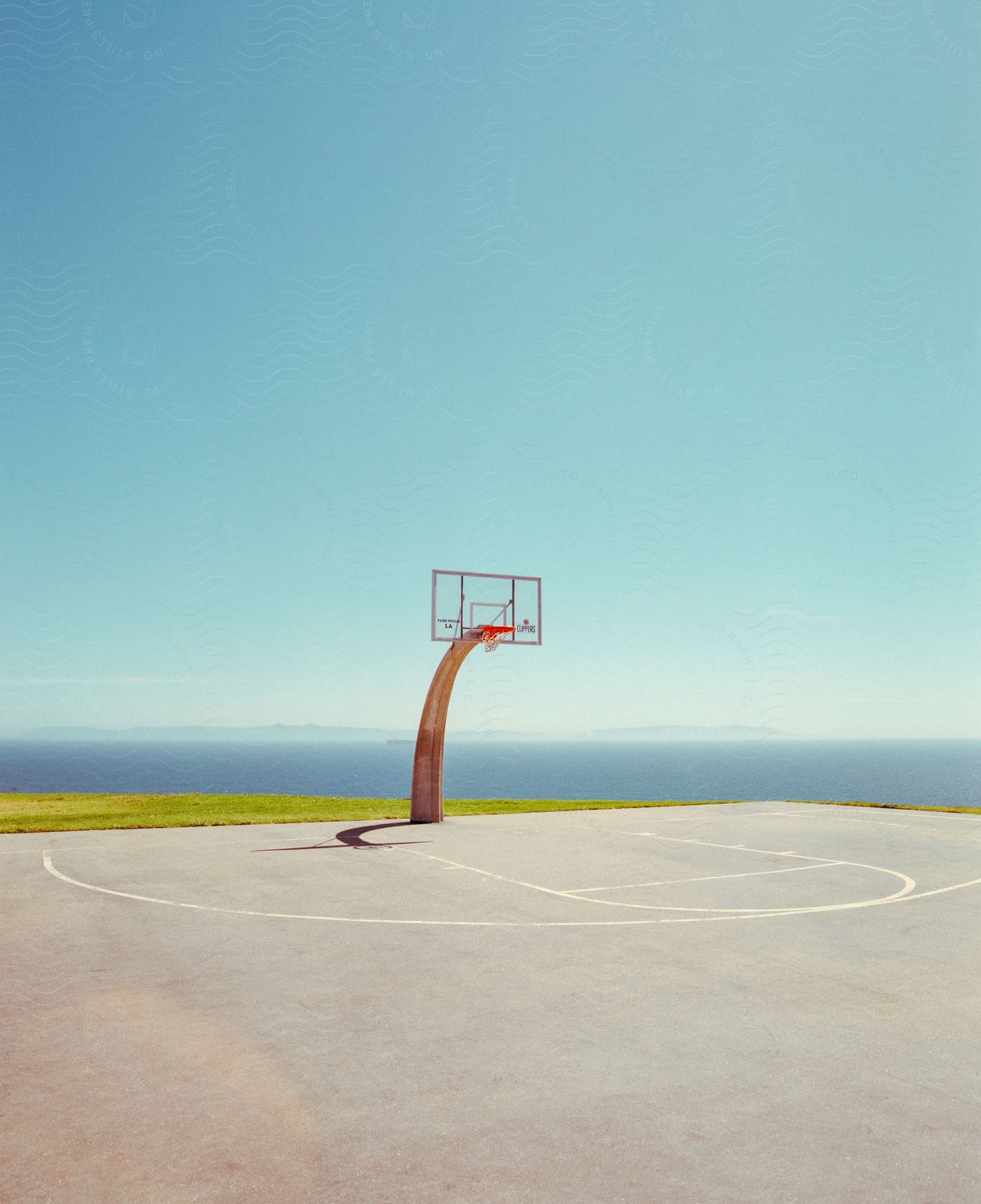 A Basketball Hoop Stands On A Coastal Court Under A Clear Sunny Sky