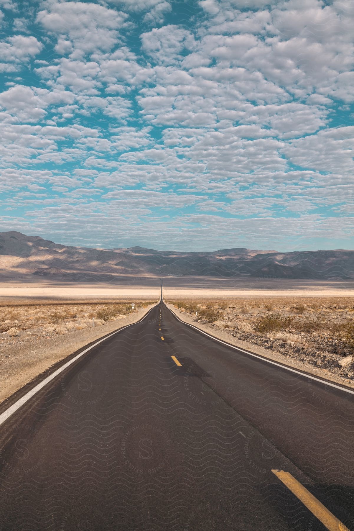 A road cuts through the desert leading to a mountain range on a cloudy day