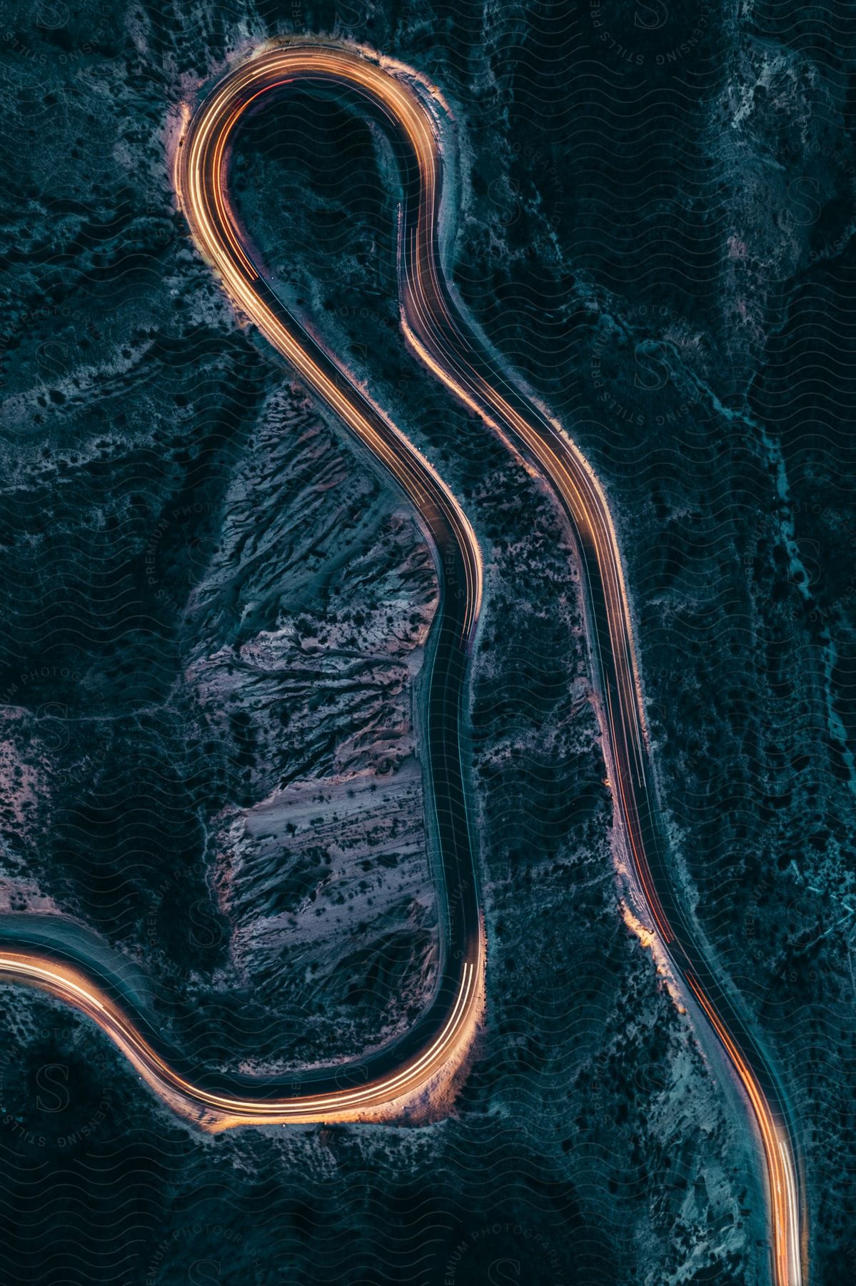 Trails of headlights illuminate a winding mountain road at night in this aerial view with a long exposure