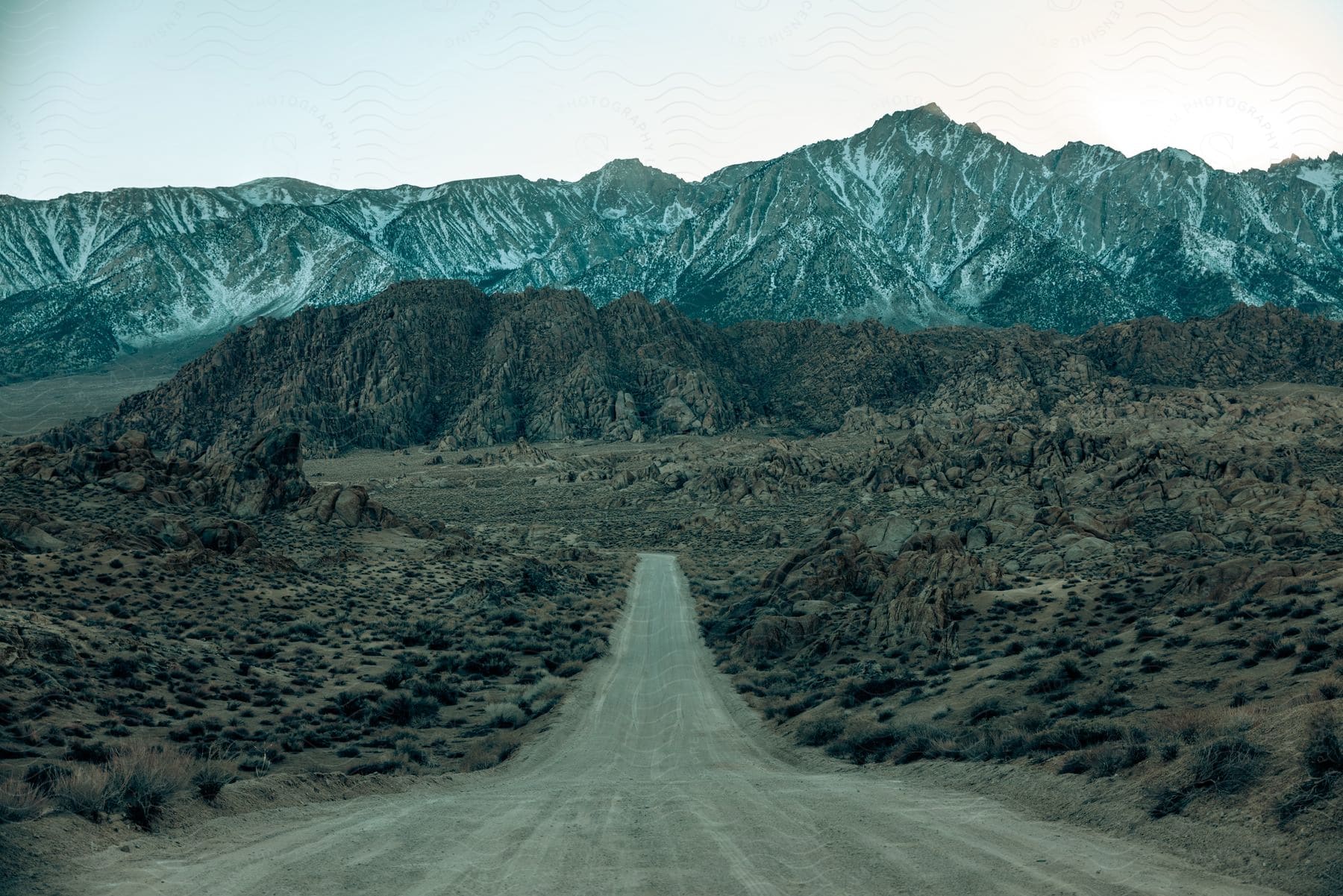 A road winds around rock covered hills and snow dusted mountains on a hazy day