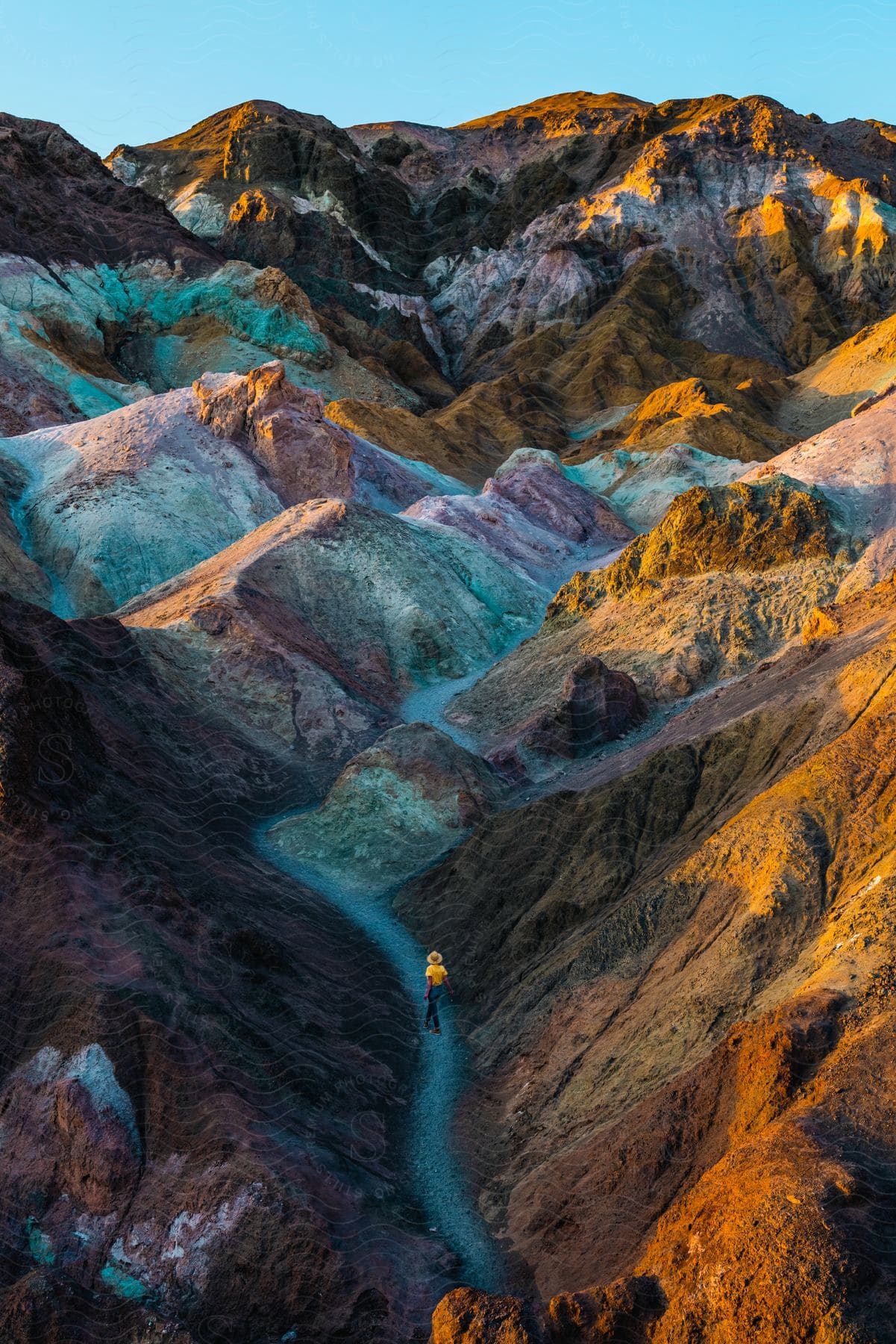 A man in yellow walks up a path through the mountains