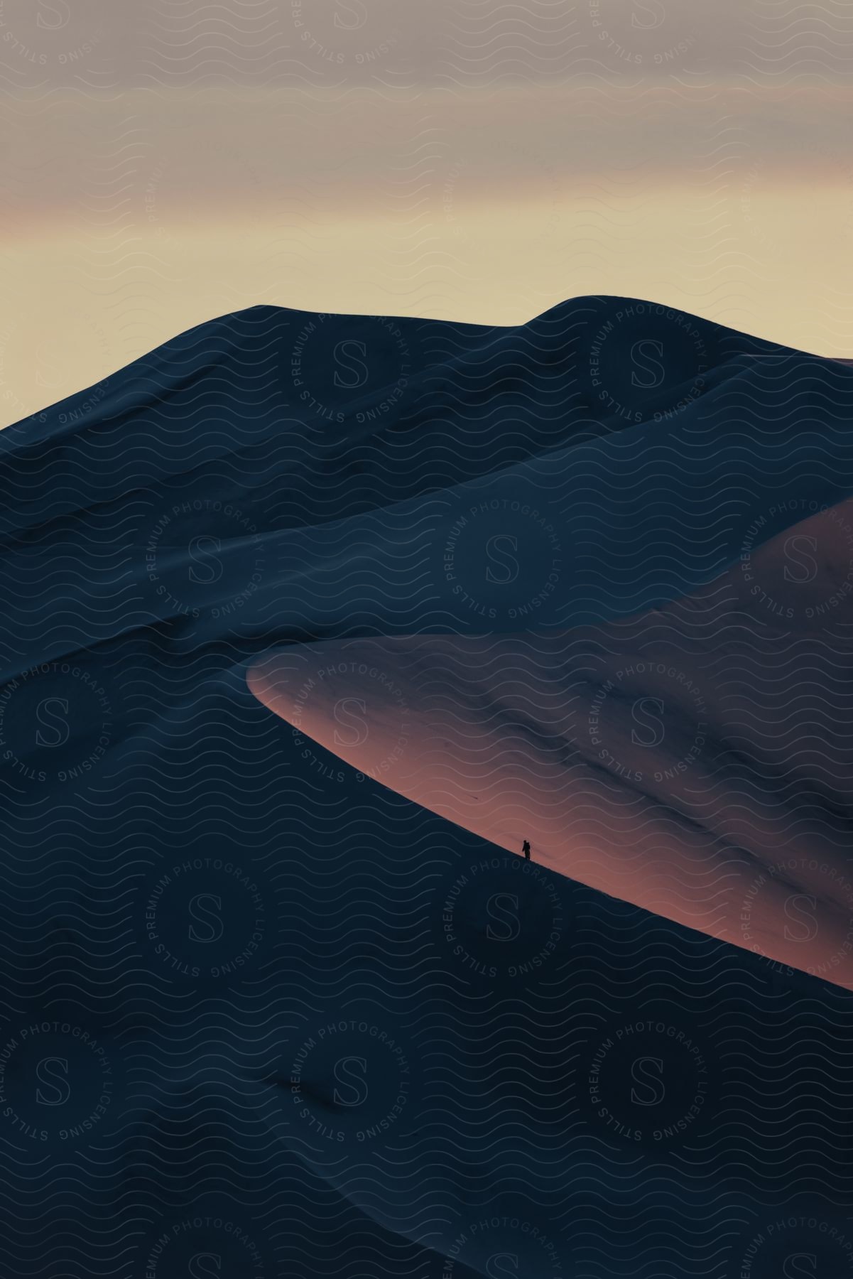 A man walking across a sand dune at sunset in the desert