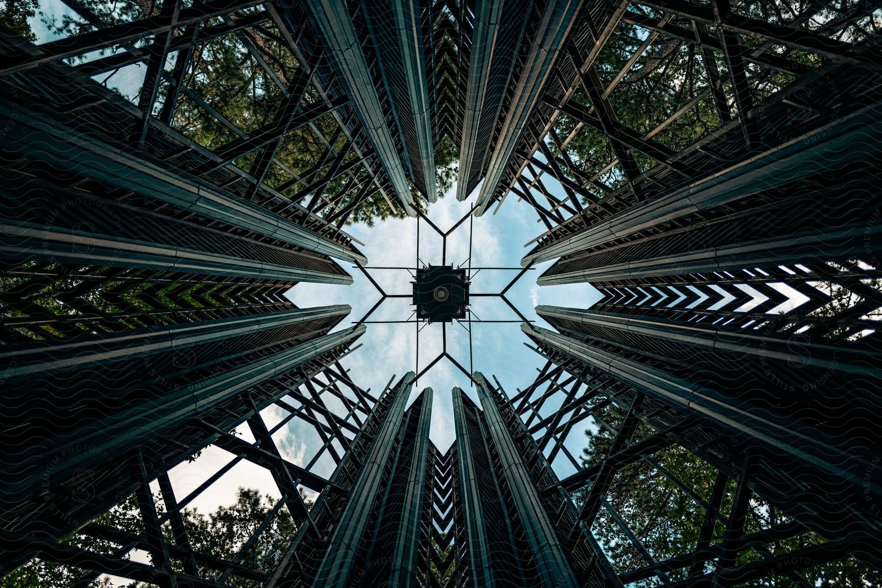 Open geometric architectural structure surrounded by trees under blue sky