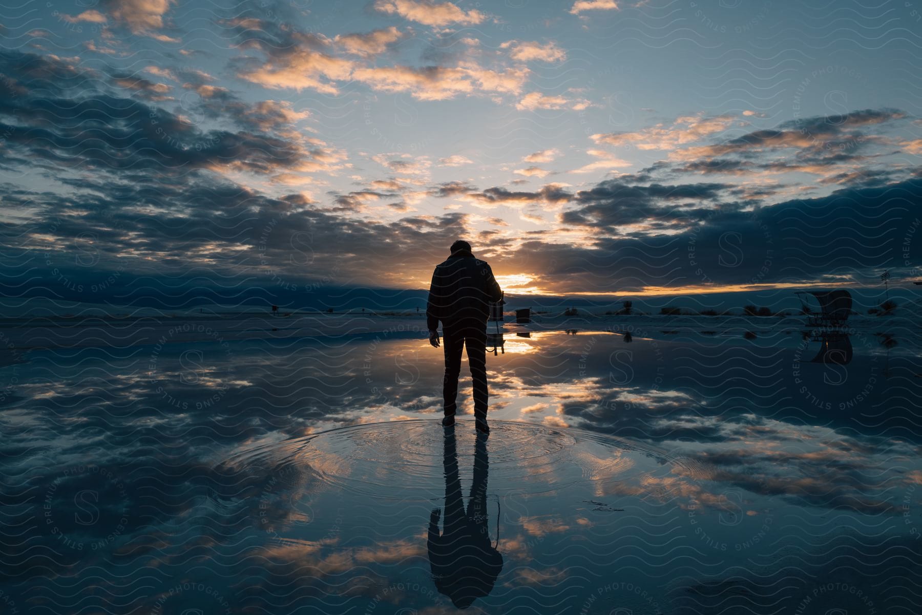 A man stands on a frozen lake at dusk with the sky and clouds in the background