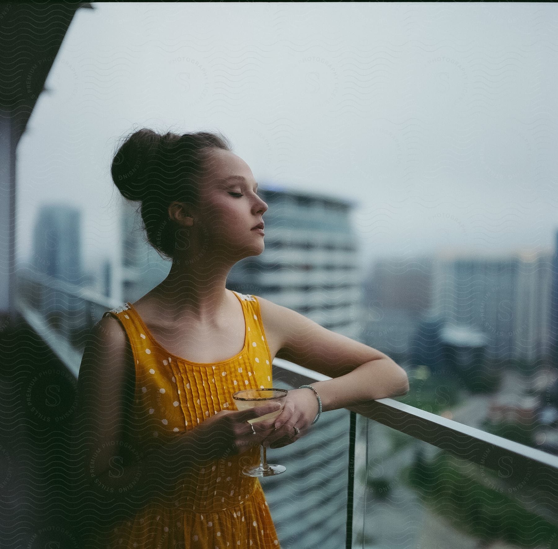 A woman in a polka dot yellow dress holds a martini glass on the balcony