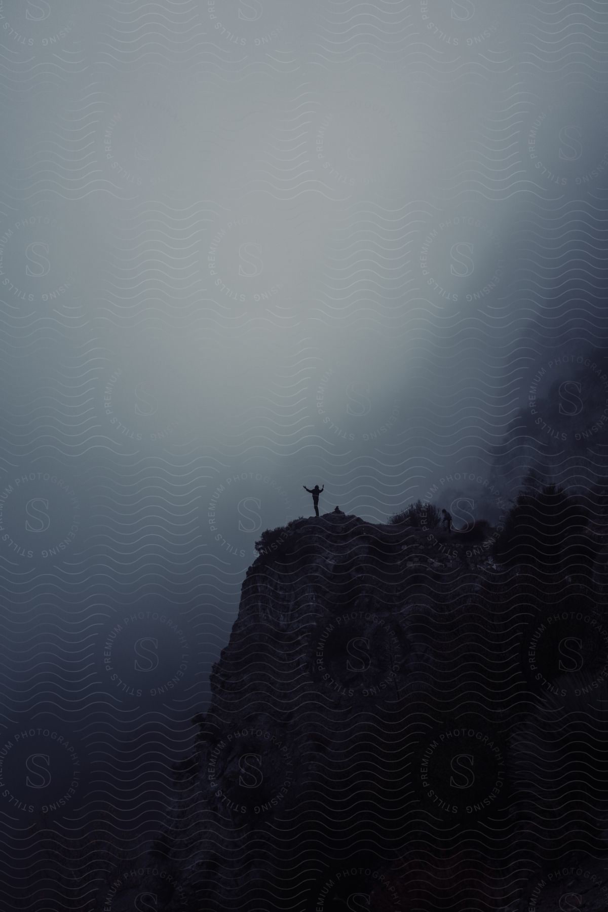 Silhouette of person standing on mountain ledge facing thick fog at dusk or dawn