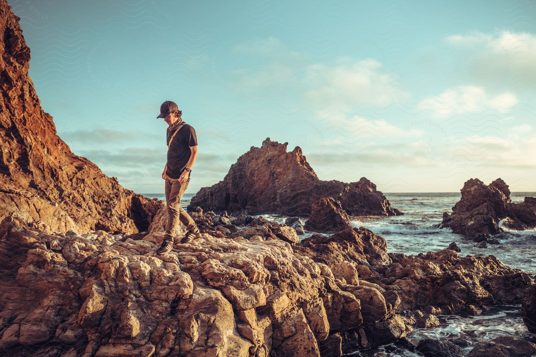 A man walks on rocky terrain along the coast near cliffs and rocks in the water as waves roll in